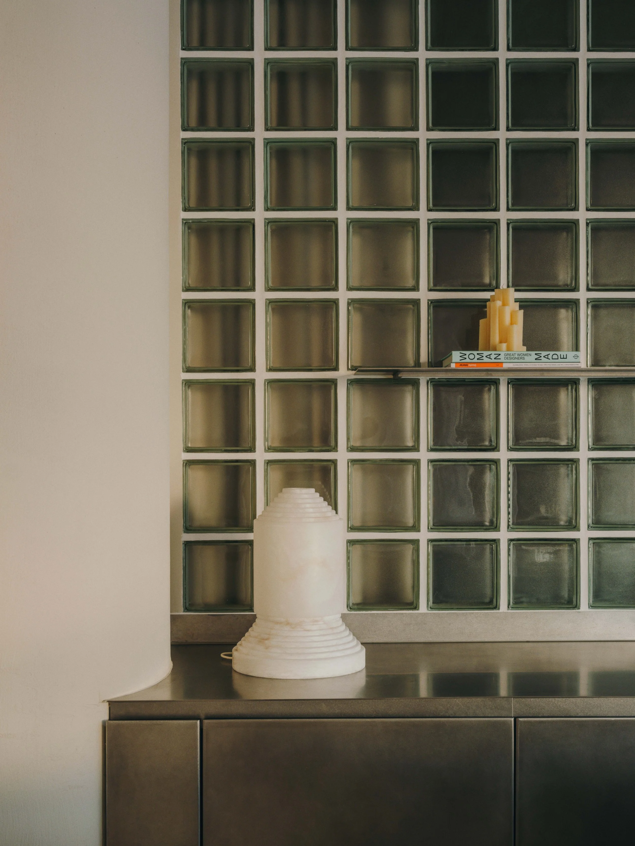 Ceramic vase and a small stack of books on a metal counter in front of glass block wall.
