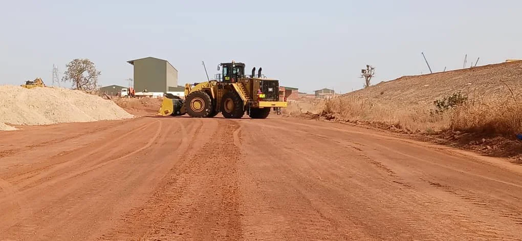 A construction site with a large yellow road grader leveling a dirt road.