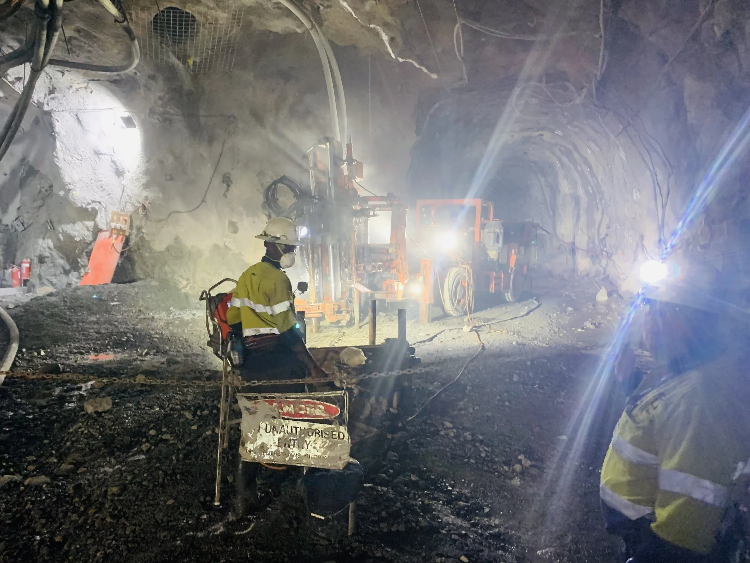 Construction workers in safety gear working inside a tunnel with heavy machinery and bright lights.