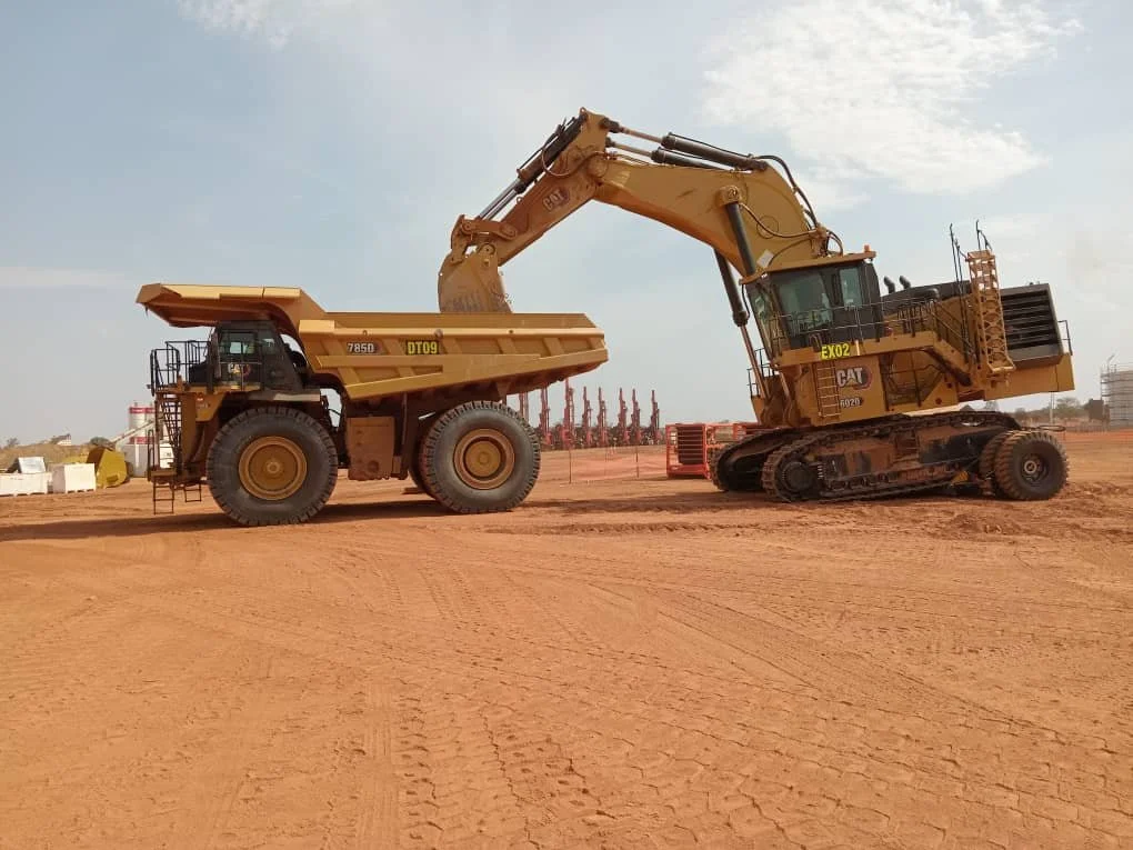 A large yellow excavator and a yellow dump truck on a dirt construction site.