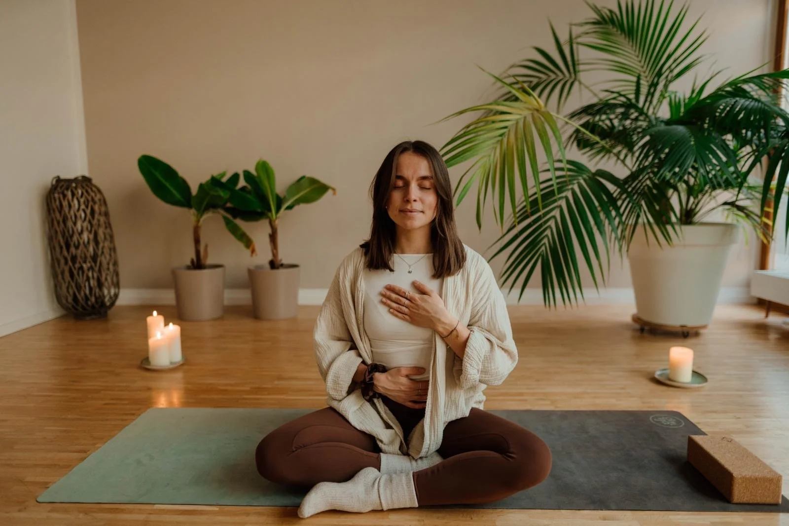Woman practicing meditation on yoga mat in a calm indoor setting, with candles and large green plants in the background.
Feeling herself and her body, connecting to her breath. Learning how to connect to her breathing again.