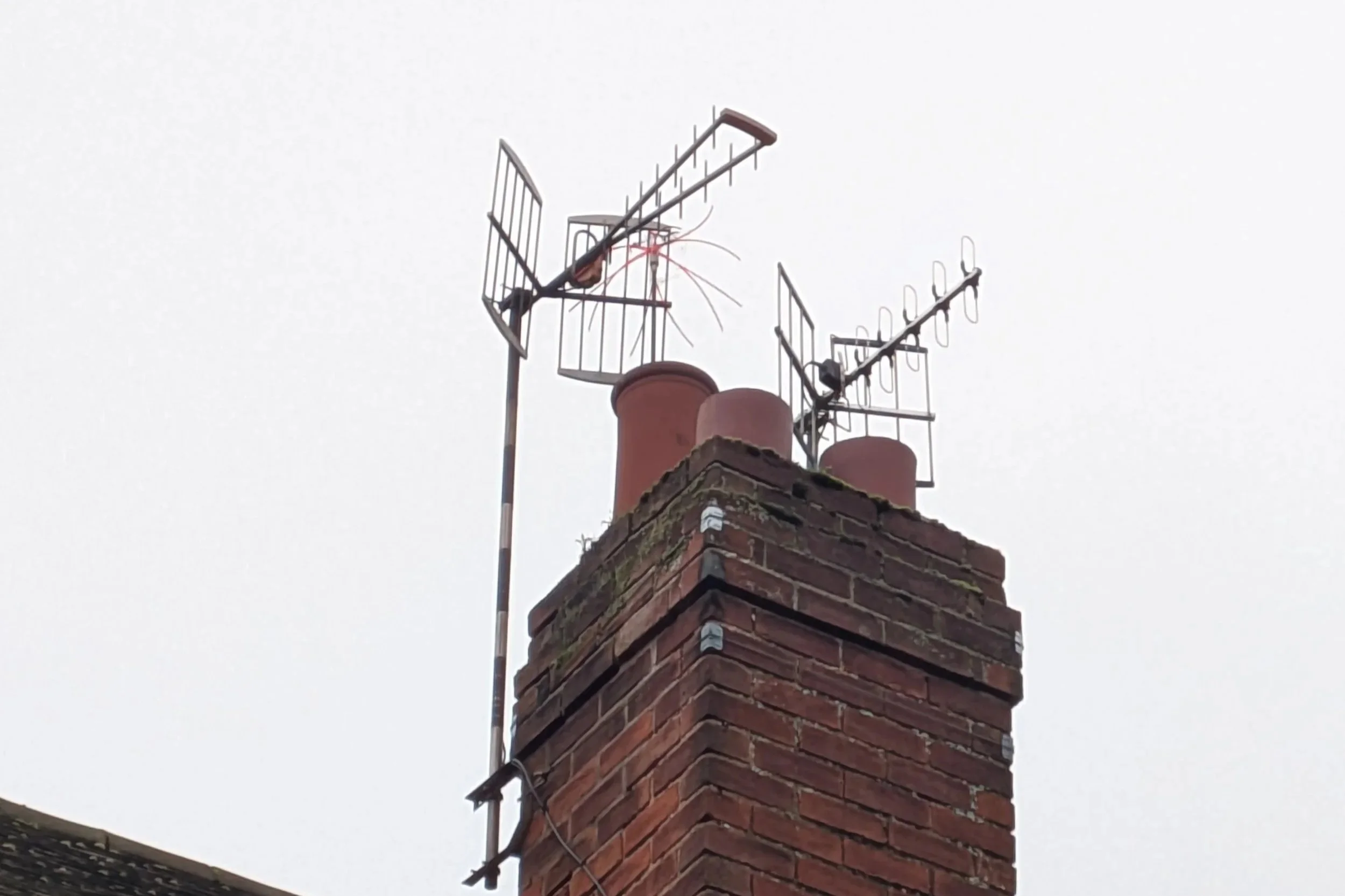 Brick chimney with three TV antennas on top, one antenna is detached and sparks are visible.