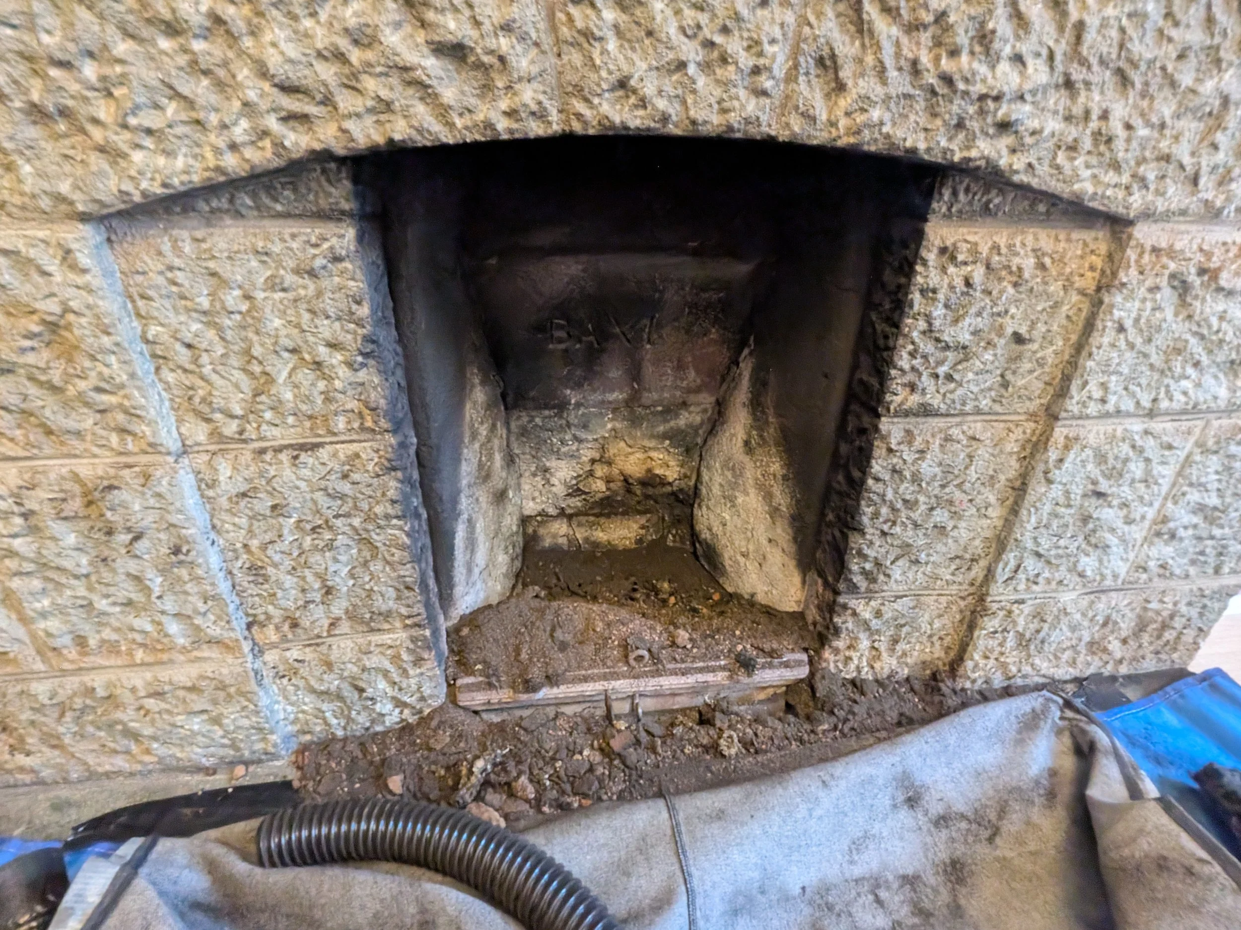 Close-up of a firebox in a brick fireplace under renovation, showing exposed bricks, soot, and a partially disassembled opening with construction debris.