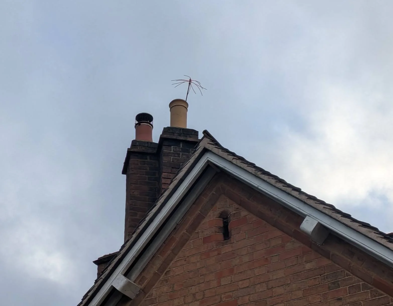View of the brick house roof, showing chimney stacks and an antenna against a cloudy sky.