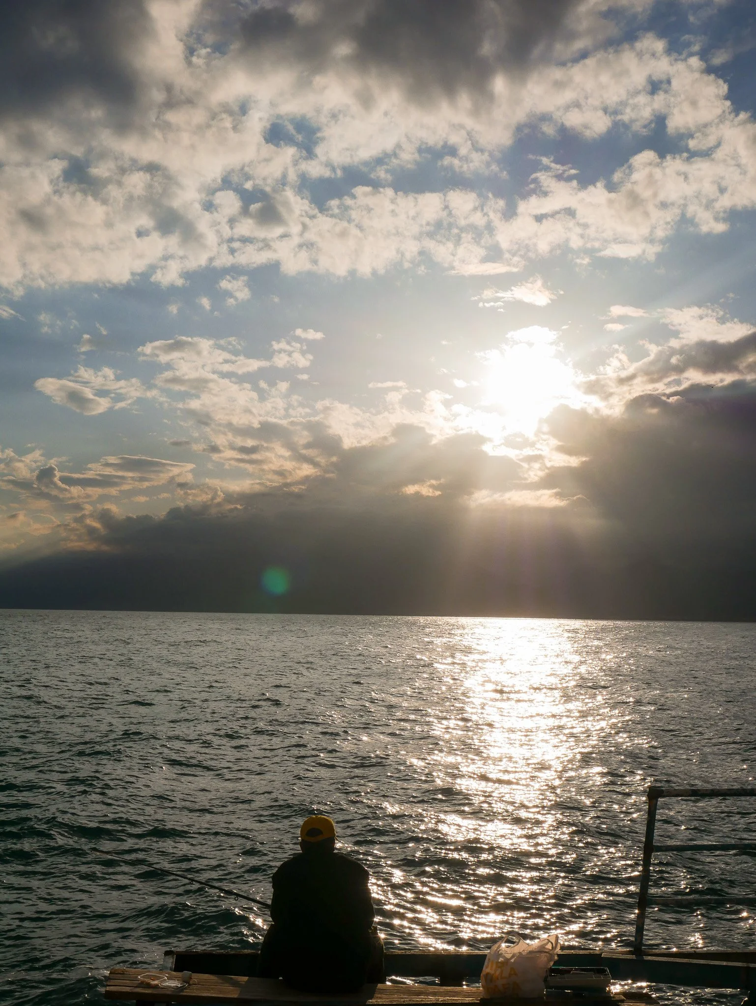 Person fishing at sunset by the water with dramatic clouds and reflected light