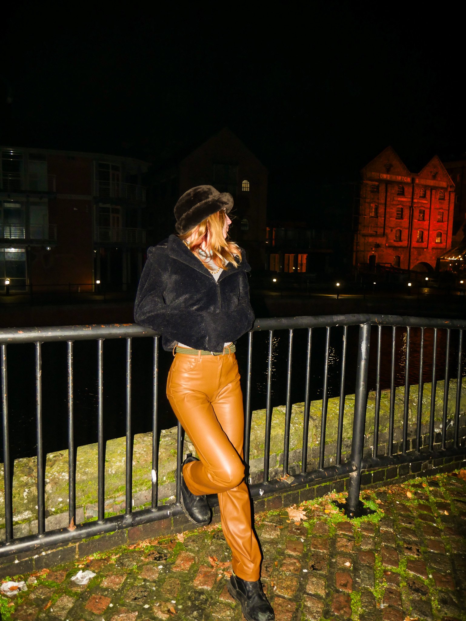 Night-time portrait of a woman standing by a riverside railing in an urban setting