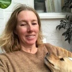 A woman with wavy blonde hair smiling while next to a golden retriever.