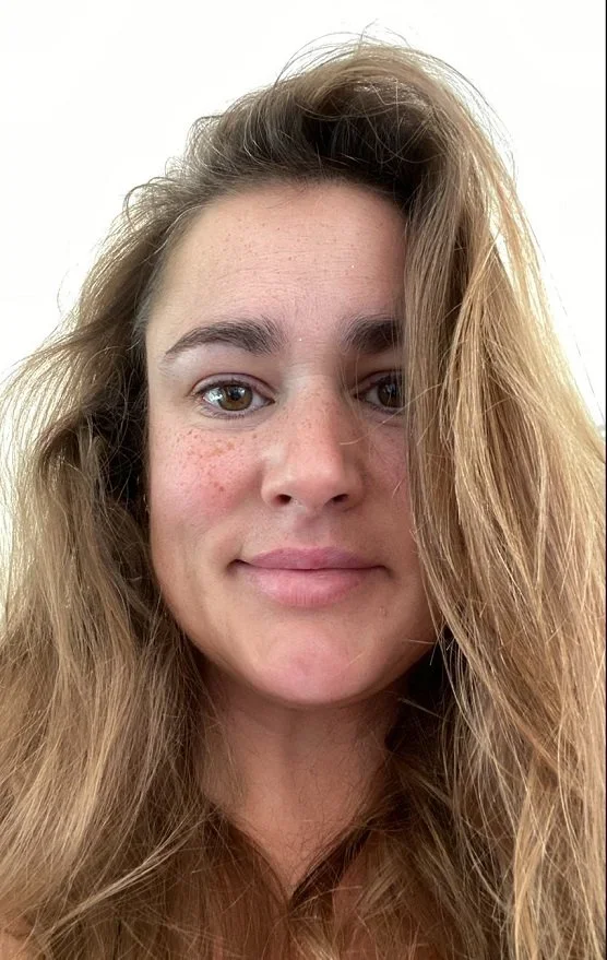 A young woman with wavy, light brown hair and fair skin, smiling gently at the camera against a plain white background.