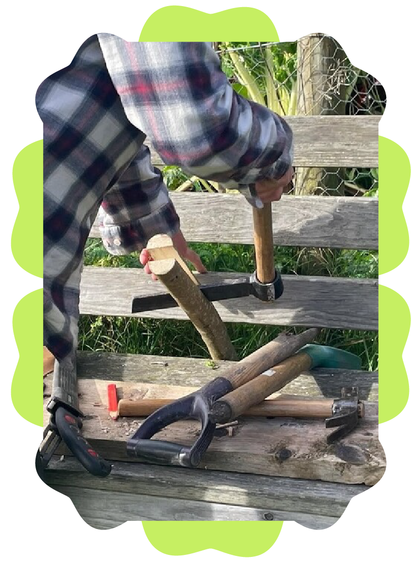 A person in a plaid shirt working with various tools on a wooden bench outdoors, with green plants and a fence in the background.