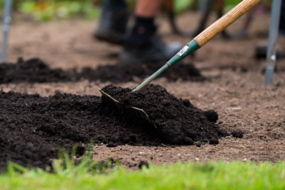 A person using a shovel to turn soil in a garden bed.