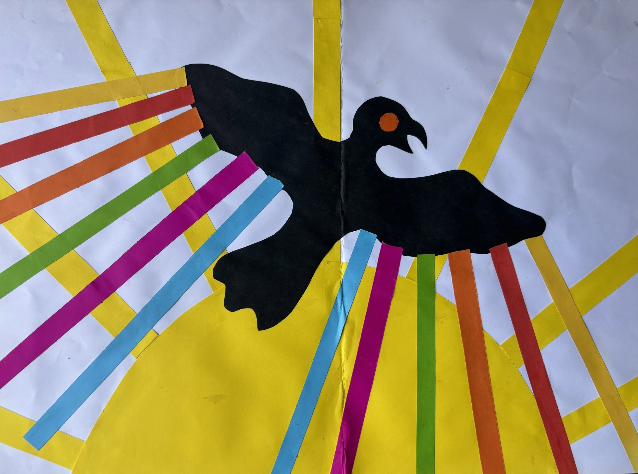 Paper craft of a black bird with an orange eye on a yellow and white background with multicolored paper strips radiating outward.