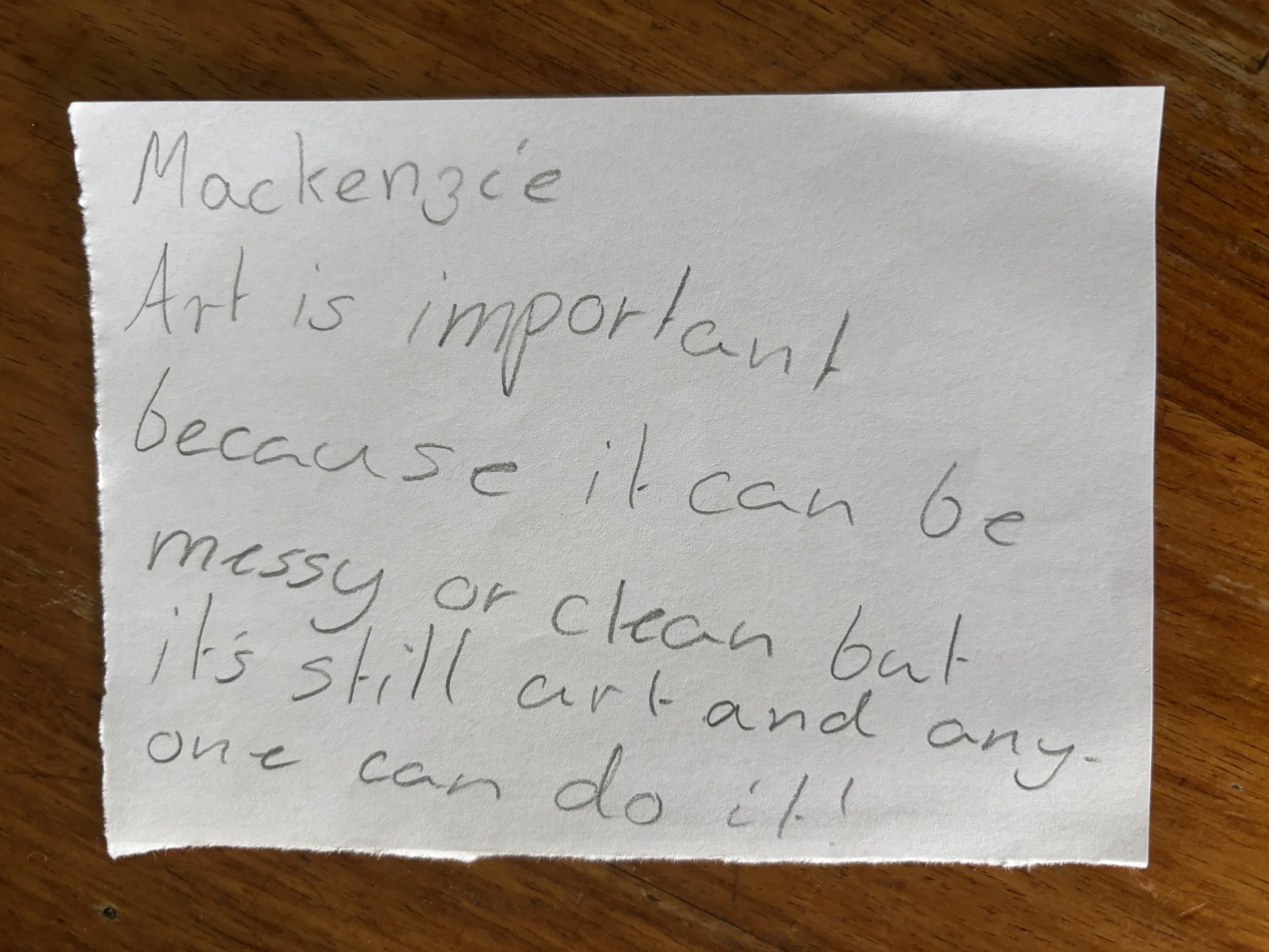 A handwritten note on a piece of paper that reads: 'Mackenzie Art is important because it can be messy or clean but it's still art and anyone can do it!'