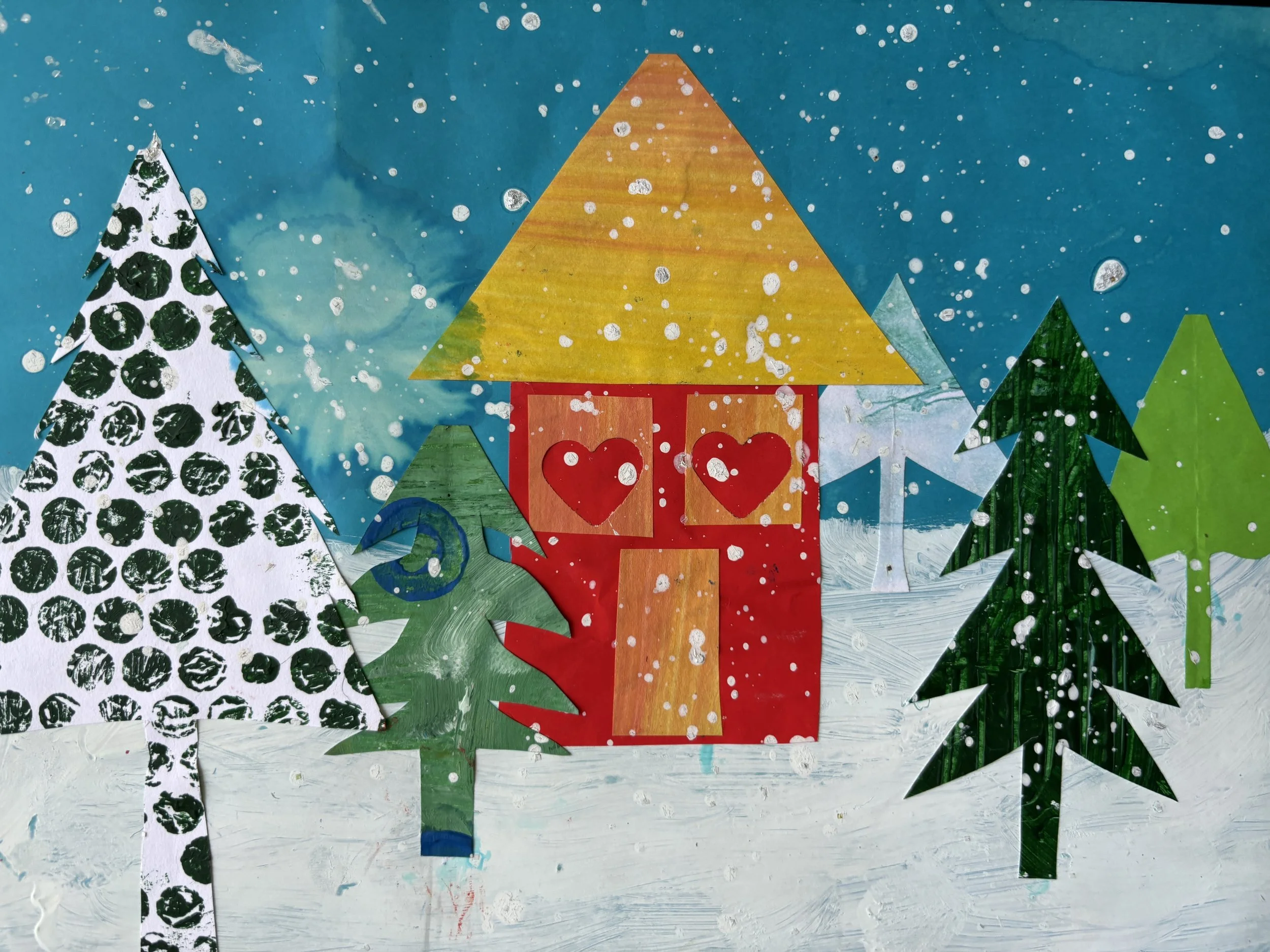 A colorful winter scene with a blue sky, snow-covered ground, and multiple stylized pine trees made from cutout paper, including a house with heart-shaped windows and a yellow roof.