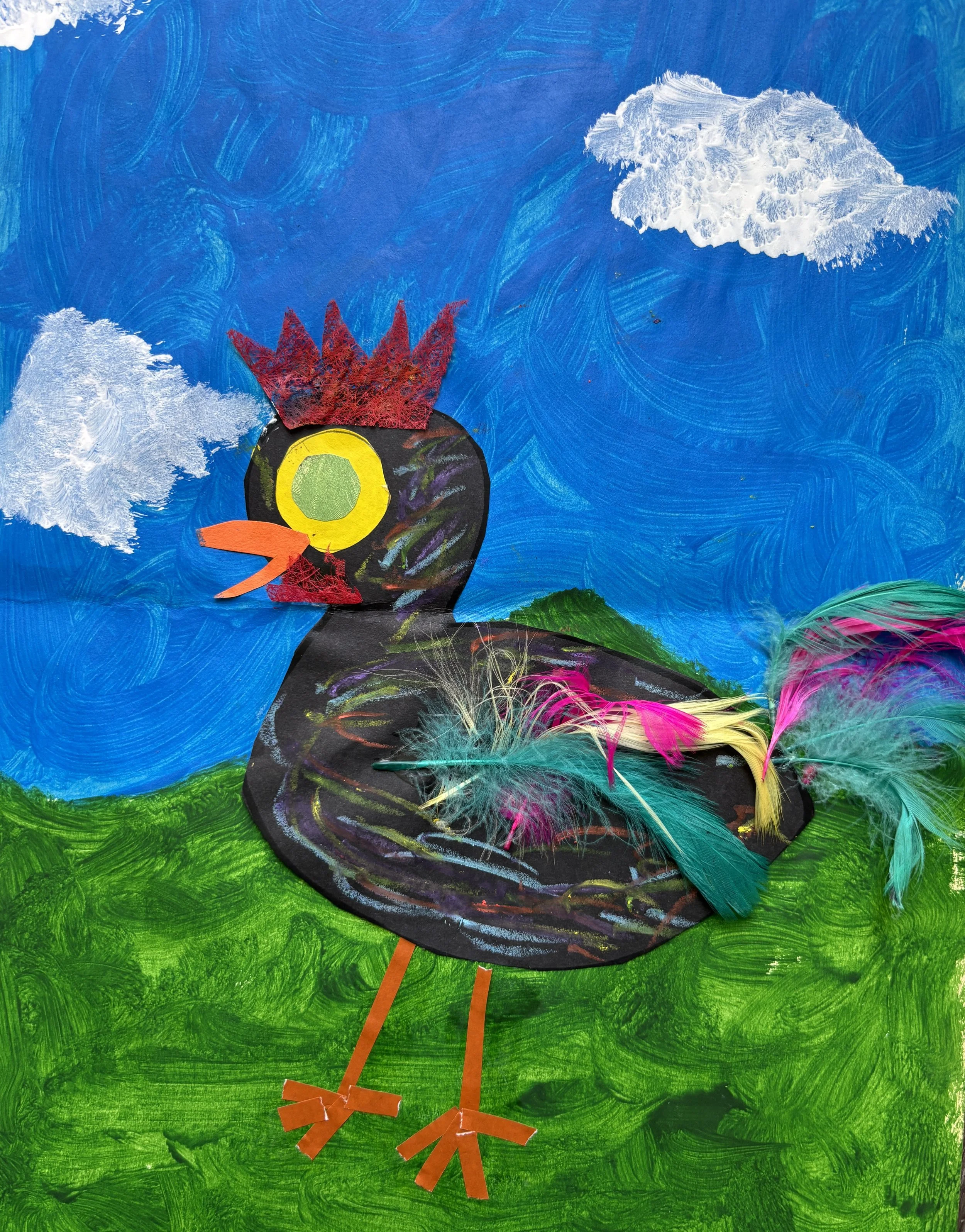 A colorful craft of a bird with feathers, using paper and feathers on a painted background of a blue sky with clouds and green grass.