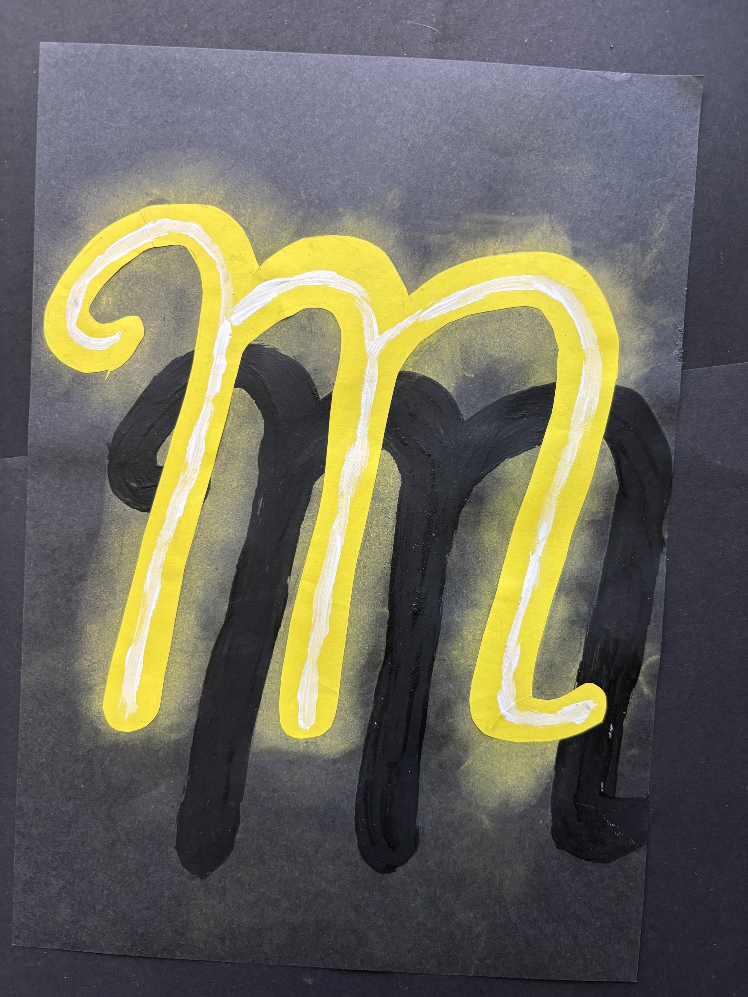 Hand-painted black and yellow outline of the letter 'M' on black paper with a yellow glow effect.