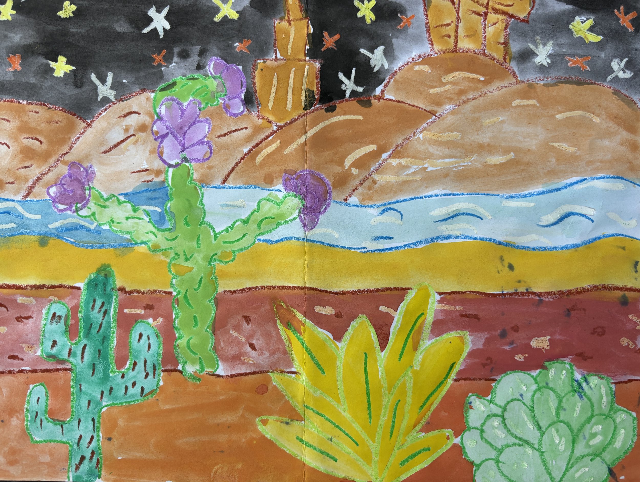 Colorful desert landscape featuring a green cactus with purple flowers, yellow and green desert plants, reddish-brown ground, blue water, brown mountains, and a dark sky with stars.