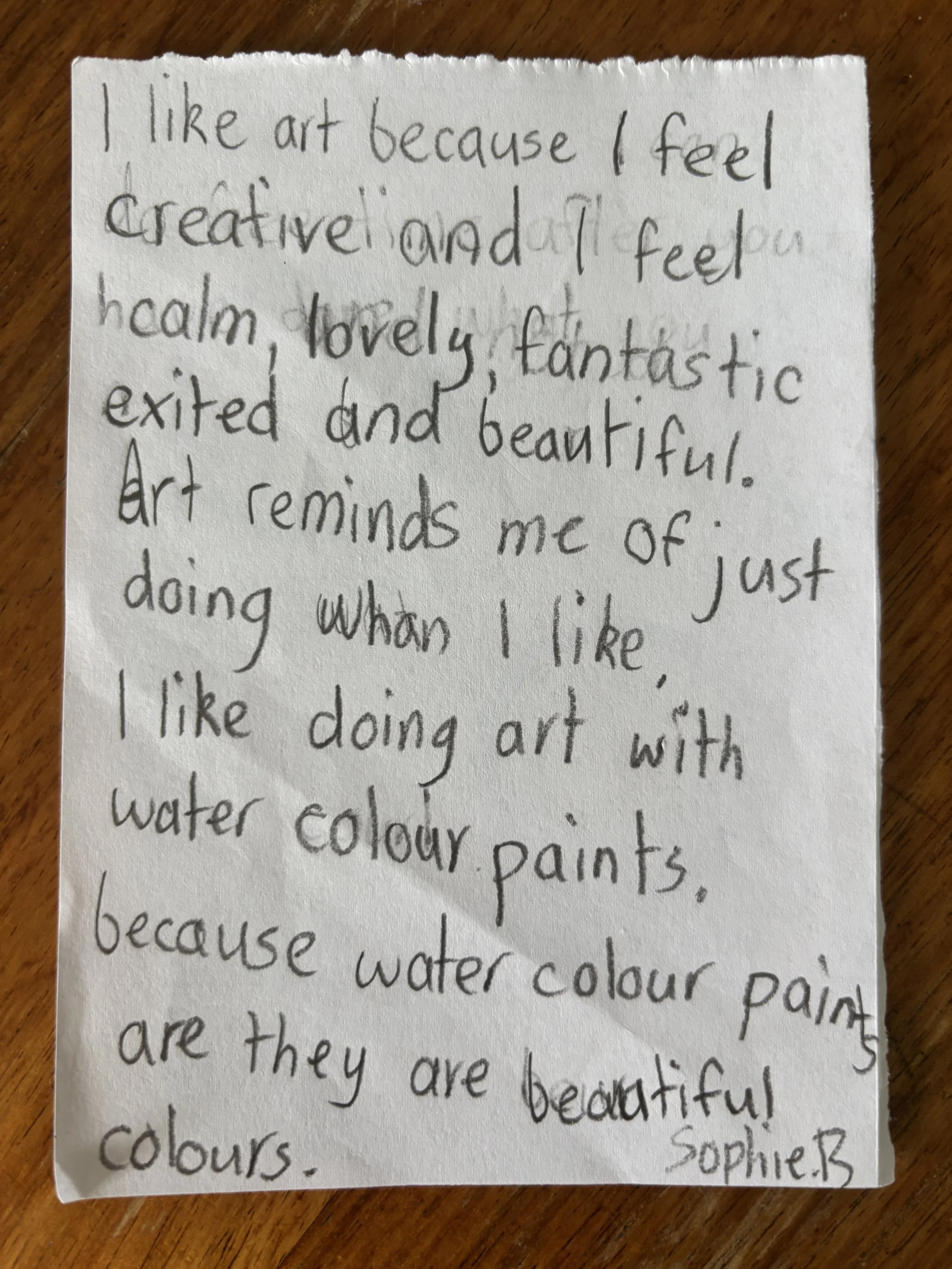 Handwritten note about liking art and water color paints with a thumbtack on a wooden surface.