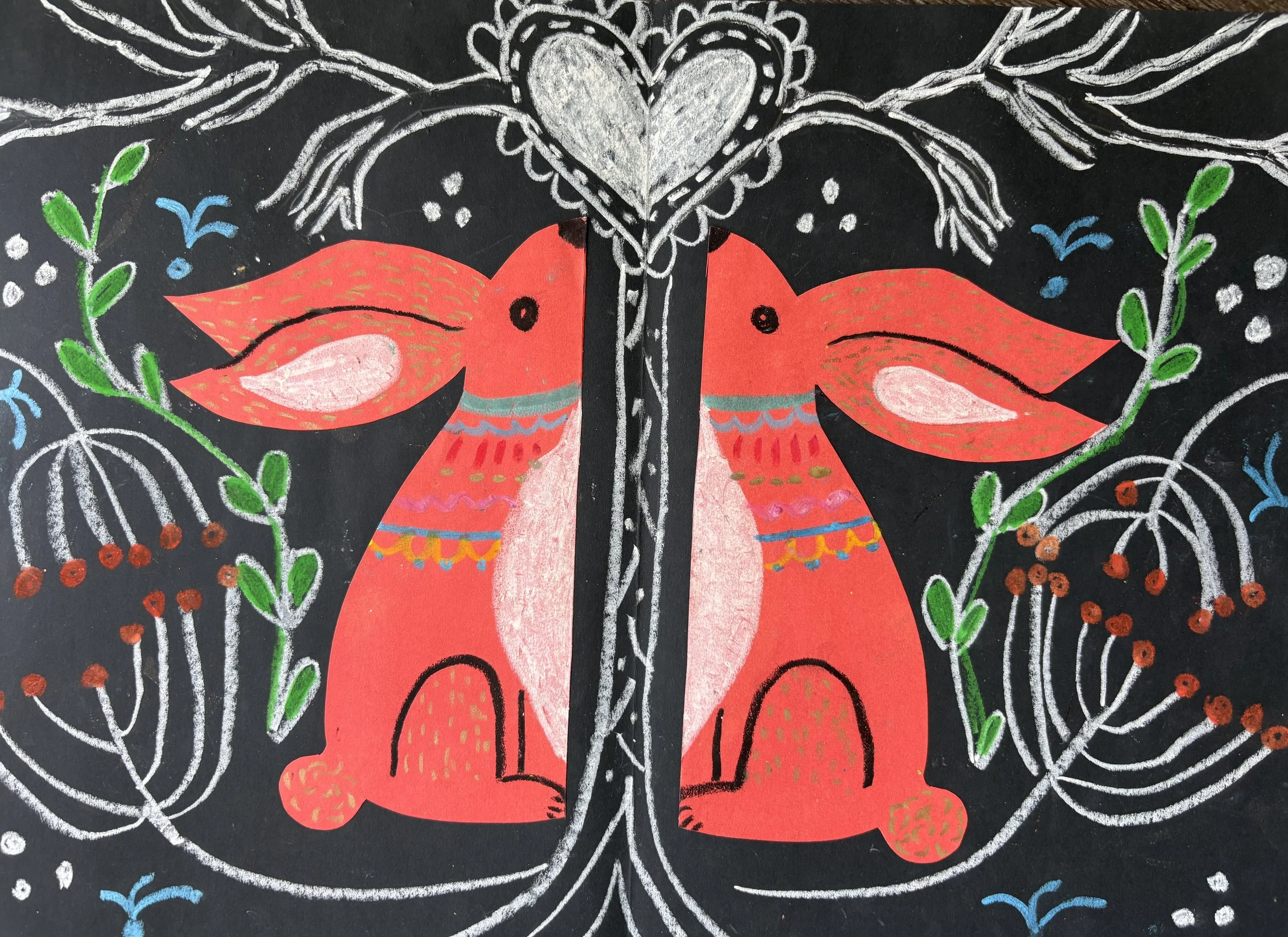 Colorful chalk drawing on black surface featuring two stylized red-orange animals facing each other, surrounded by white swirling lines, green leaves, red berries, blue accents, and a heart shape at the top center.
