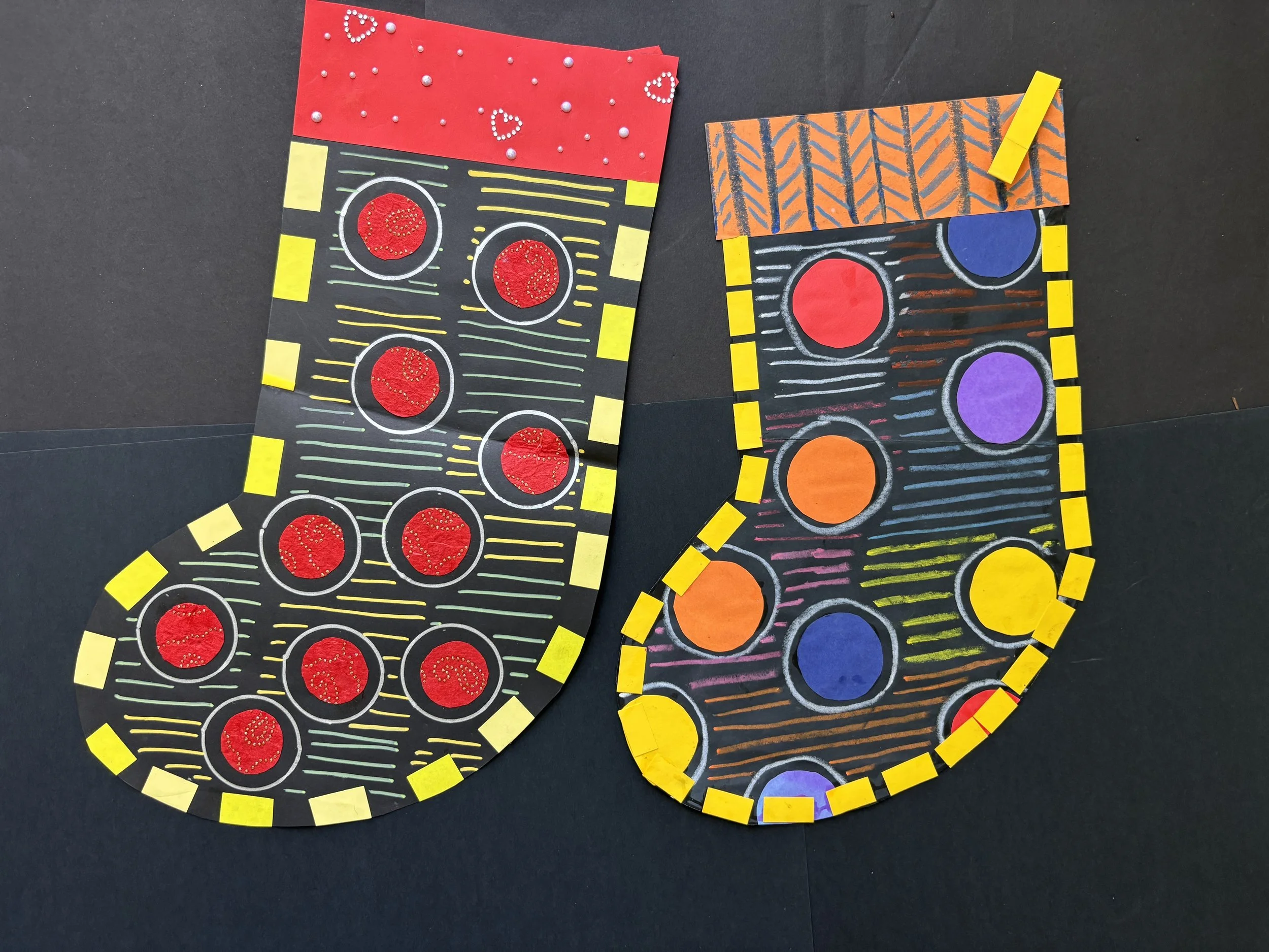 Colorful Christmas stockings craft with black backgrounds, decorated with colored paper circles, stripes, and yellow-bordered edge patterns.