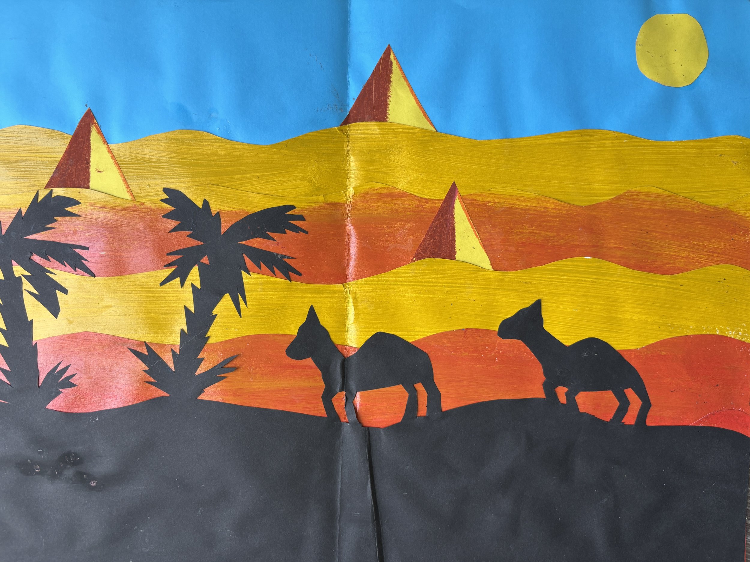 Silhouette of two camels and desert plants against a colorful sunset with pyramids and a yellow sun in the background.