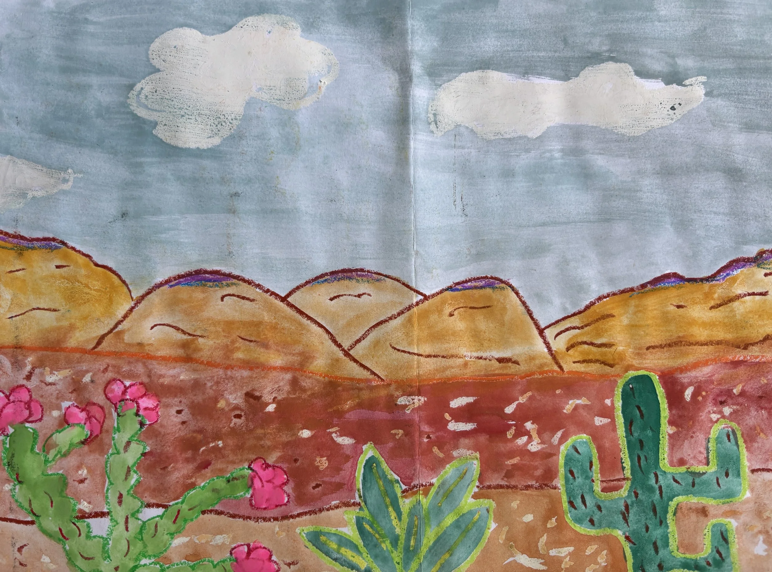 Children's drawing of a desert landscape with mountains, cacti, and a cave, under a blue sky with clouds.