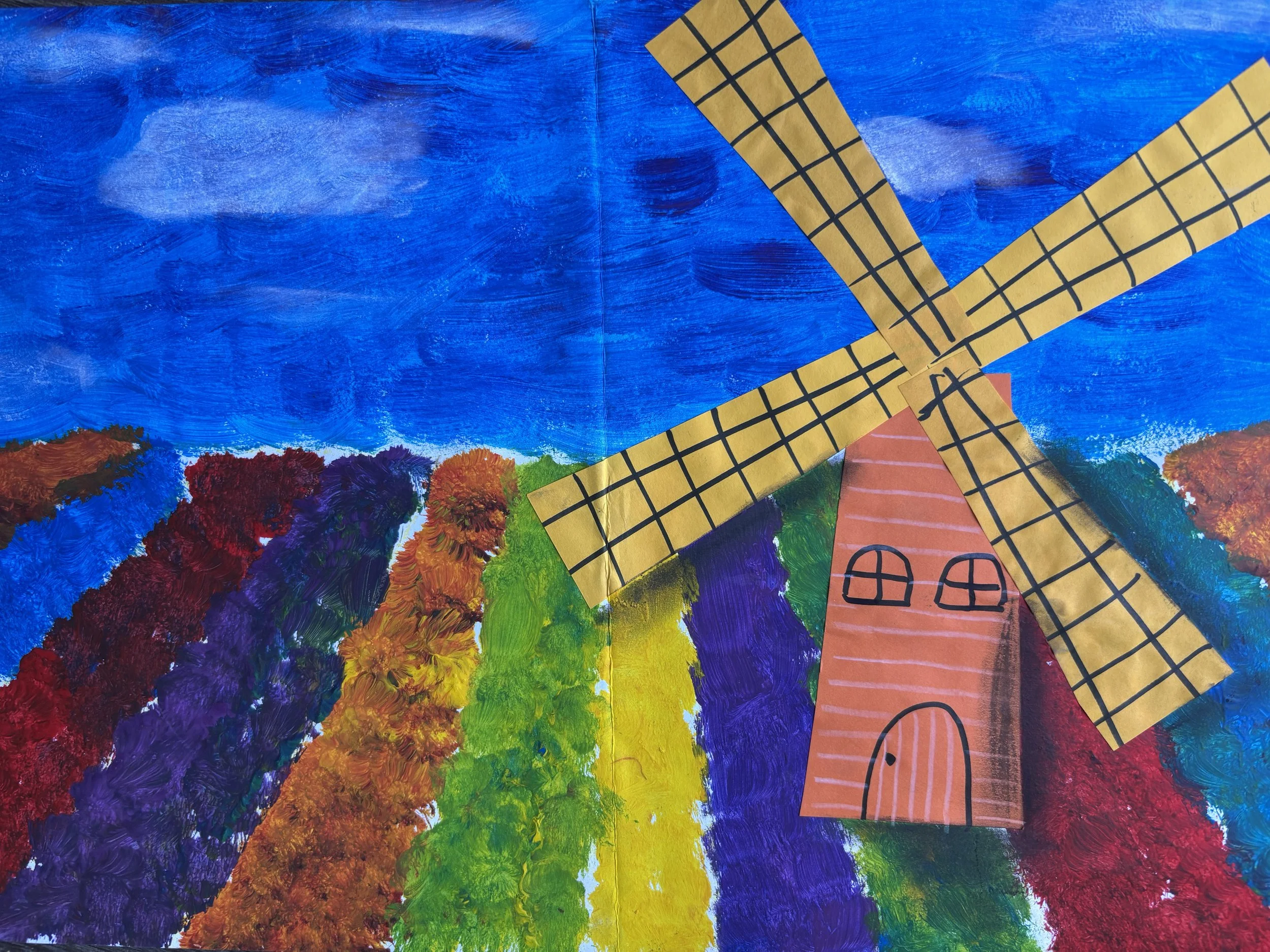 Colorful painting of a windmill with a pink body and yellow blades, set against a vibrant rainbow sky and multicolored fields of flowers.