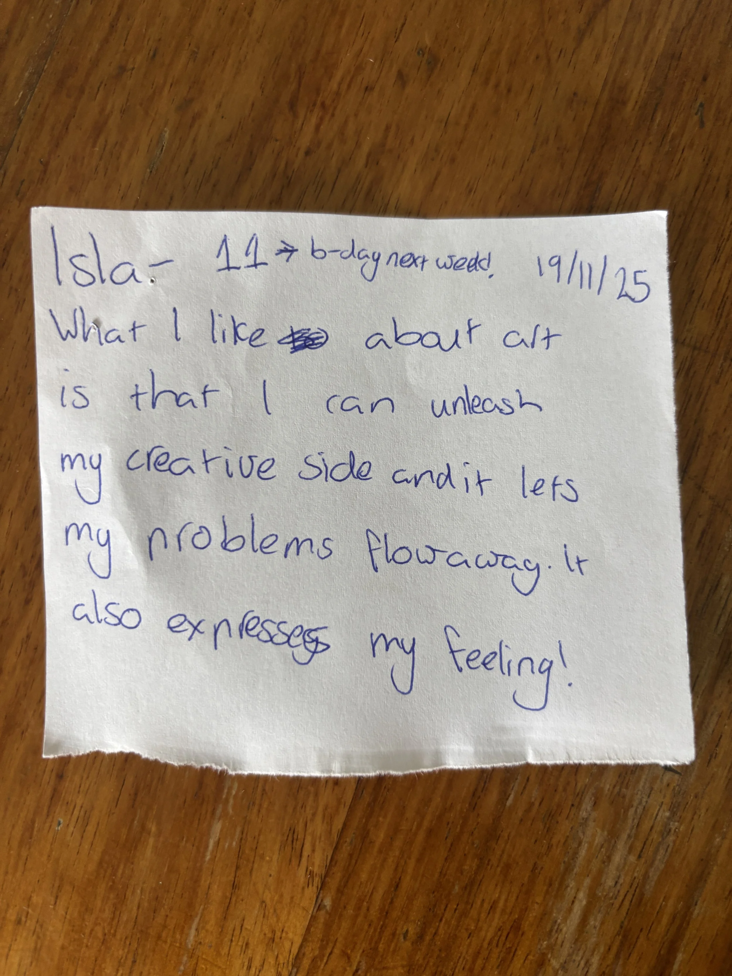 Handwritten note on a torn piece of paper with blue ink, placed on a wooden surface.