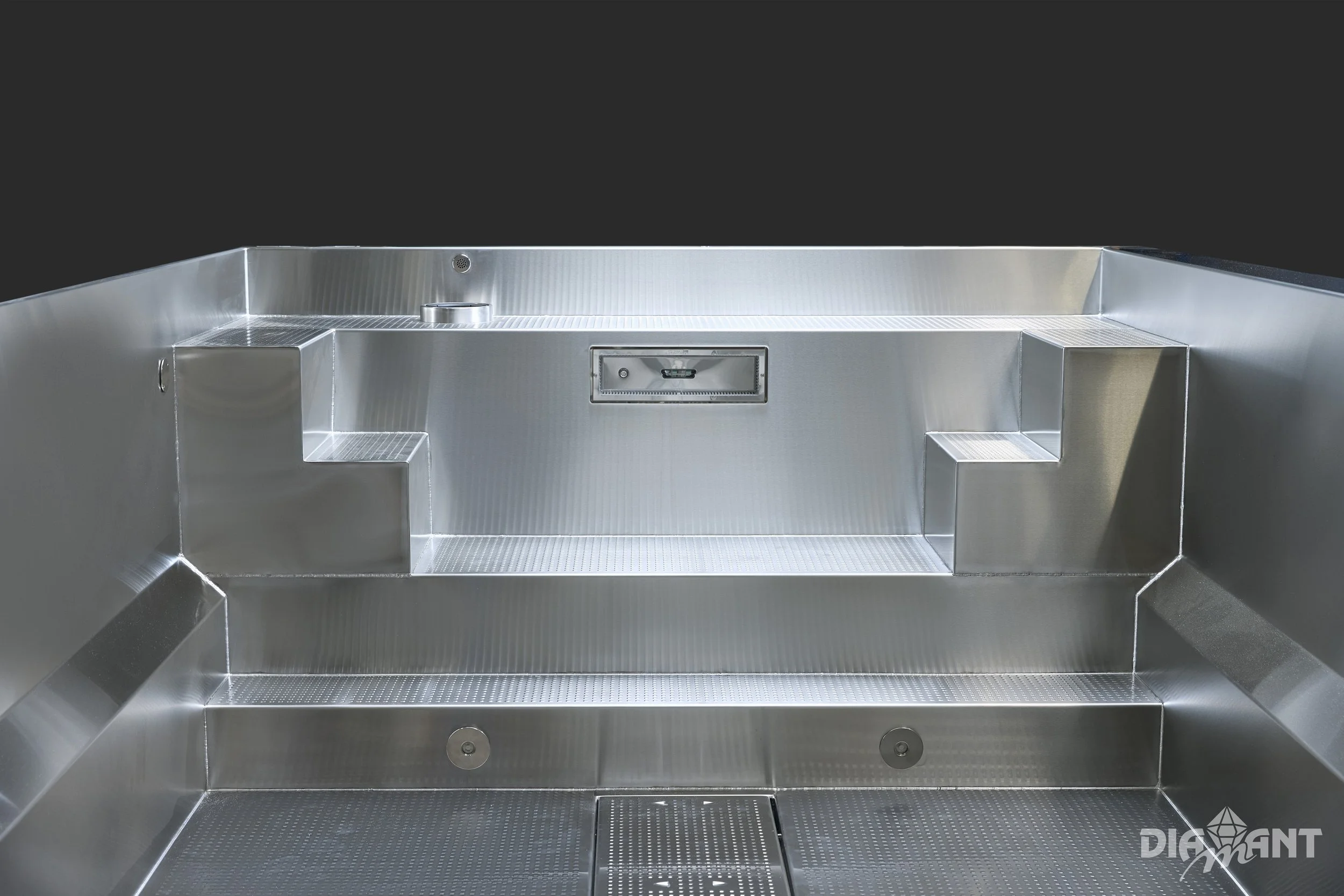 Close-up of a modern metallic outdoor grill with built-in step stools, a grill cover, and a black background.