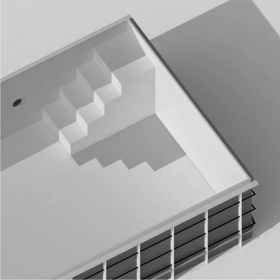 Top view of a modern indoor swimming pool with an L-shaped design, featuring steps in the corner and black lounge chairs along the side.