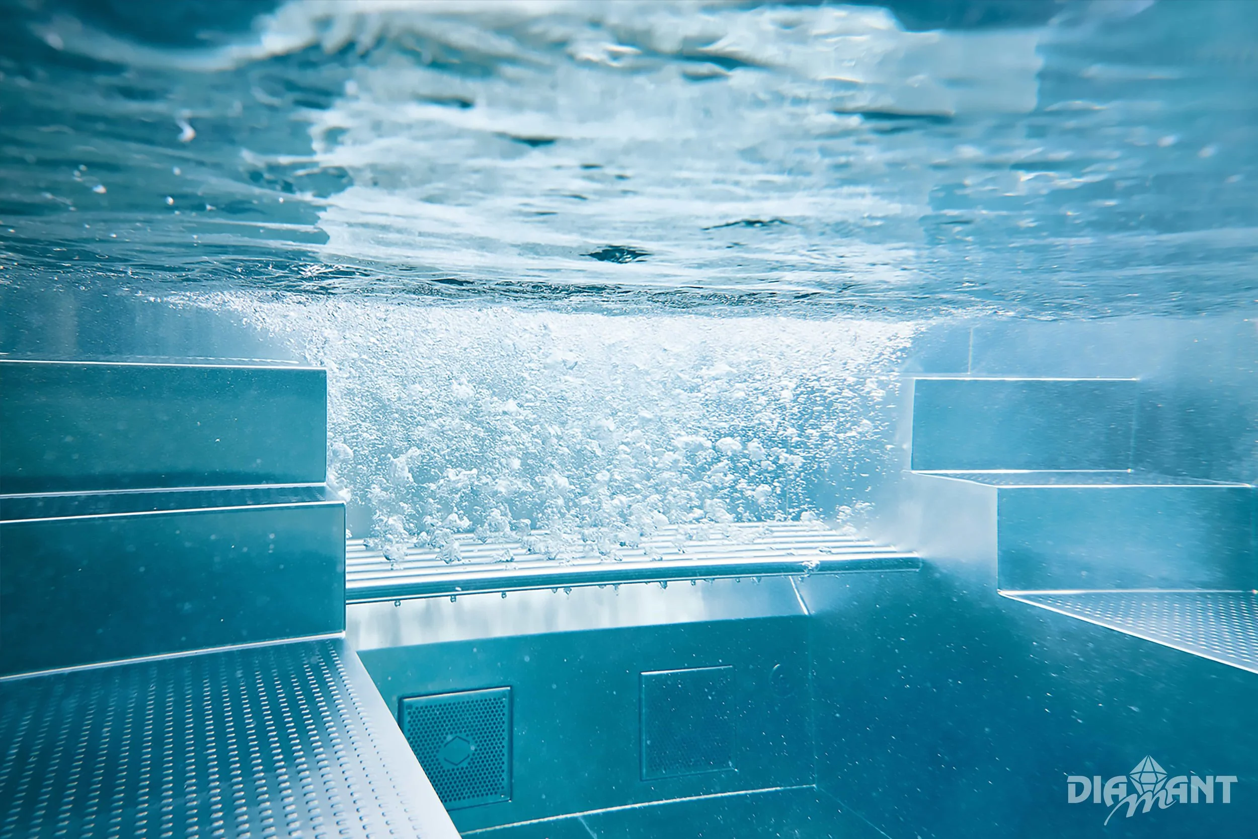 Underwater view of a swimming pool with steps and bubbling water, taken from below the surface.