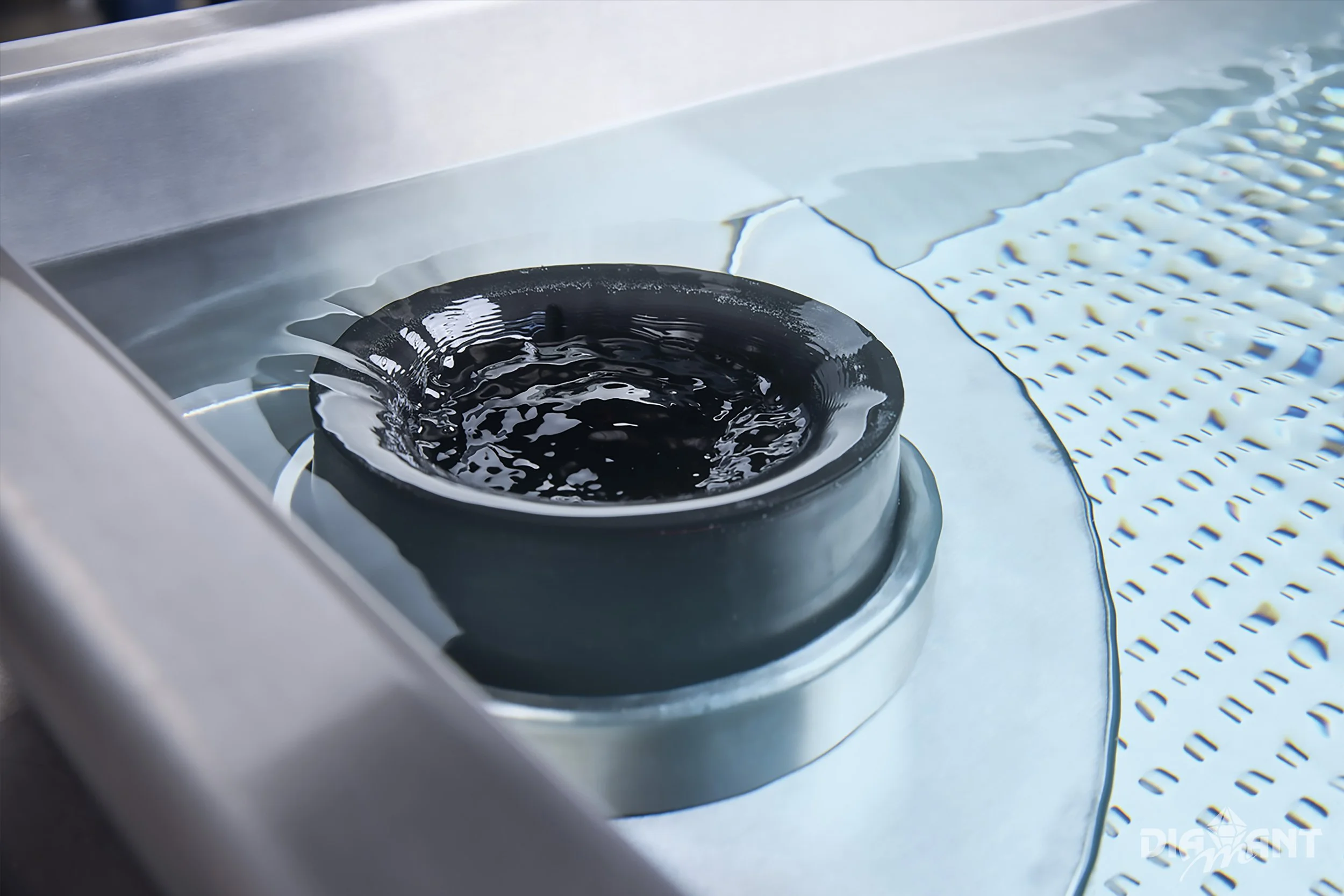 Close-up of a black rubber O-ring seal submerged in water inside a metal tank, with a patterned surface nearby.