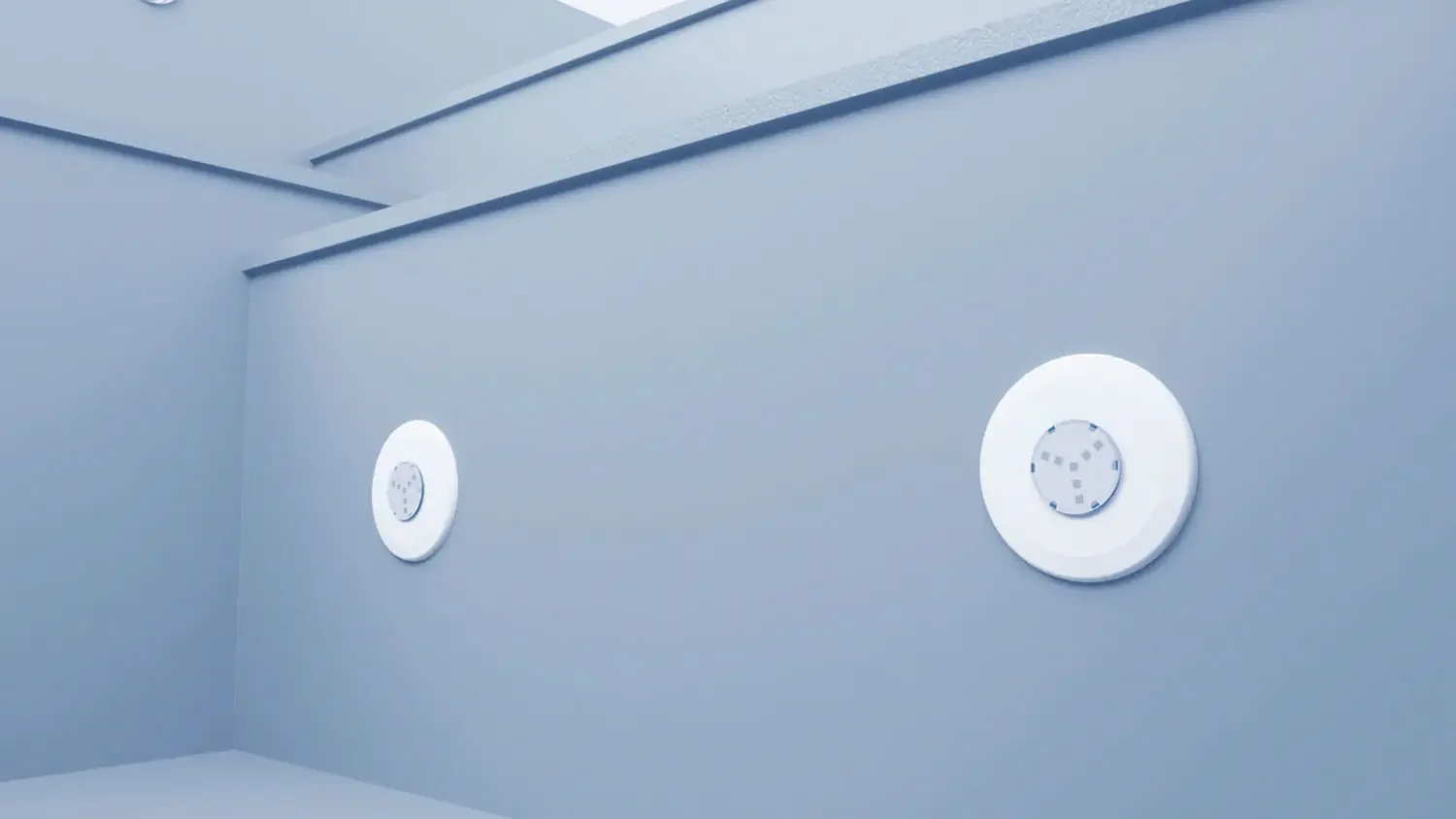 Two circular devices mounted on a light gray wall in an indoor setting.