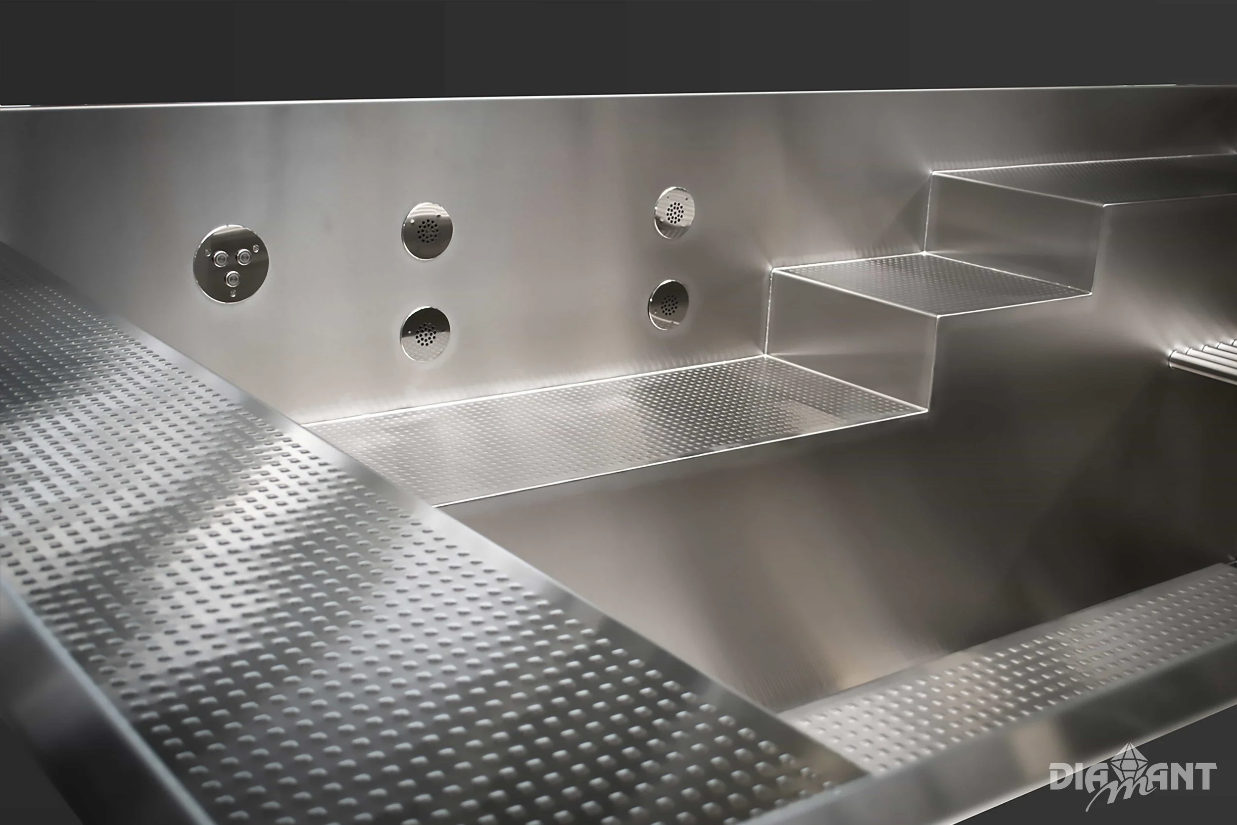 Close-up of a stainless steel kitchen sink with multiple spray nozzles, textured drainboard, and a logo reading 'DIGANT' in the bottom right corner.