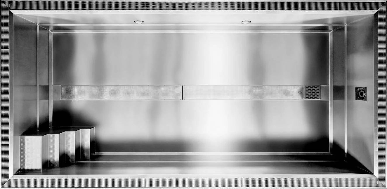 Empty stainless steel elevator interior with a small platform step at the bottom left corner and ceiling lights.