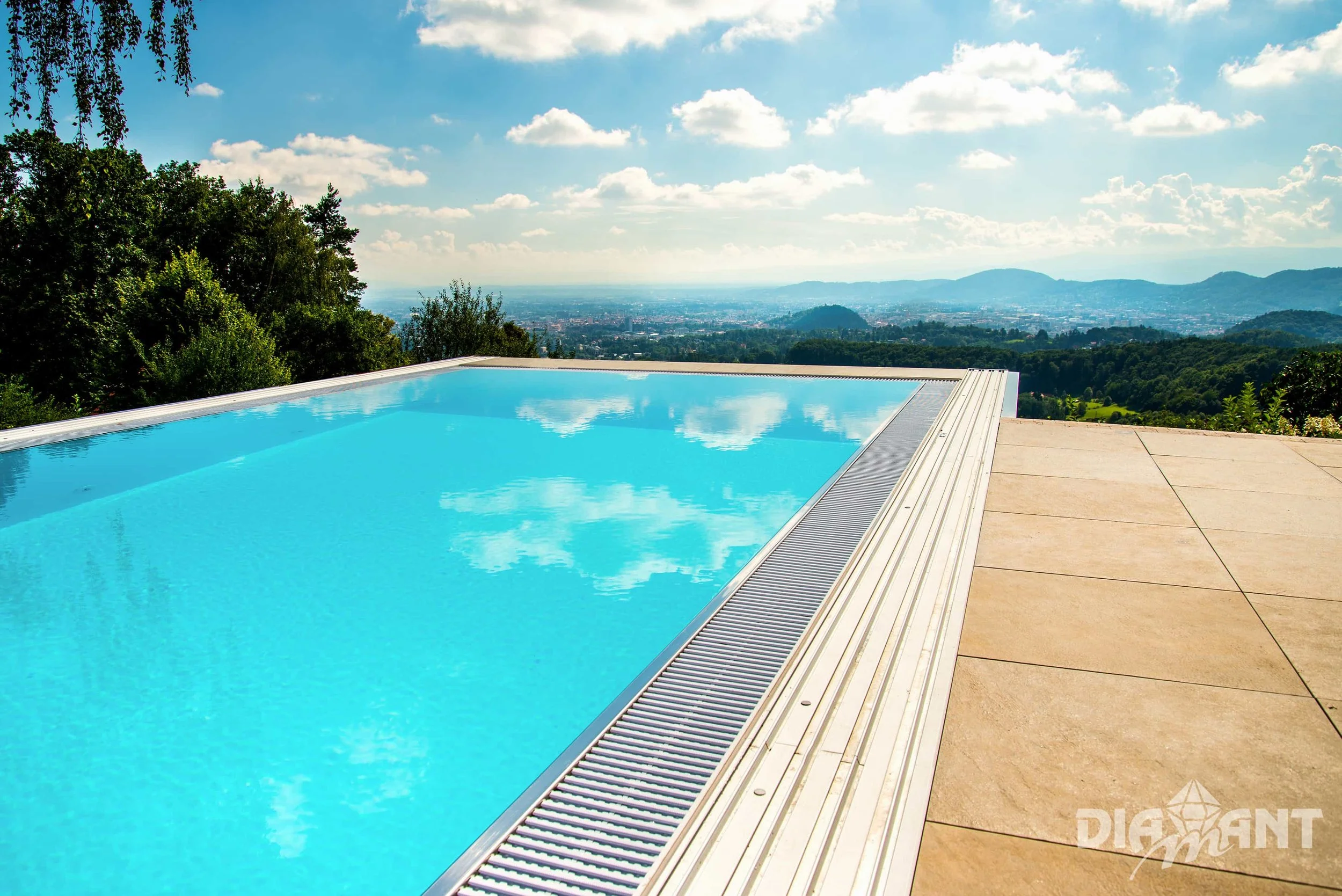 Infinity pool overlooking a scenic landscape with mountains, trees, and a cloudy sky.