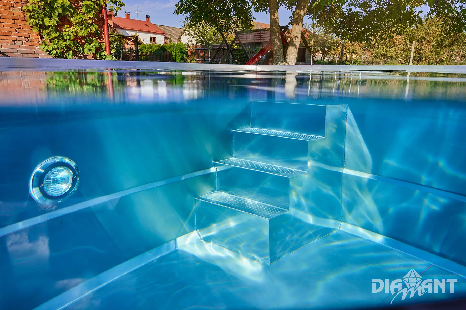 Empty sparkling swimming pool with metallic stairs and underwater lighting, outdoor backyard with trees and houses in the background, sunny day.