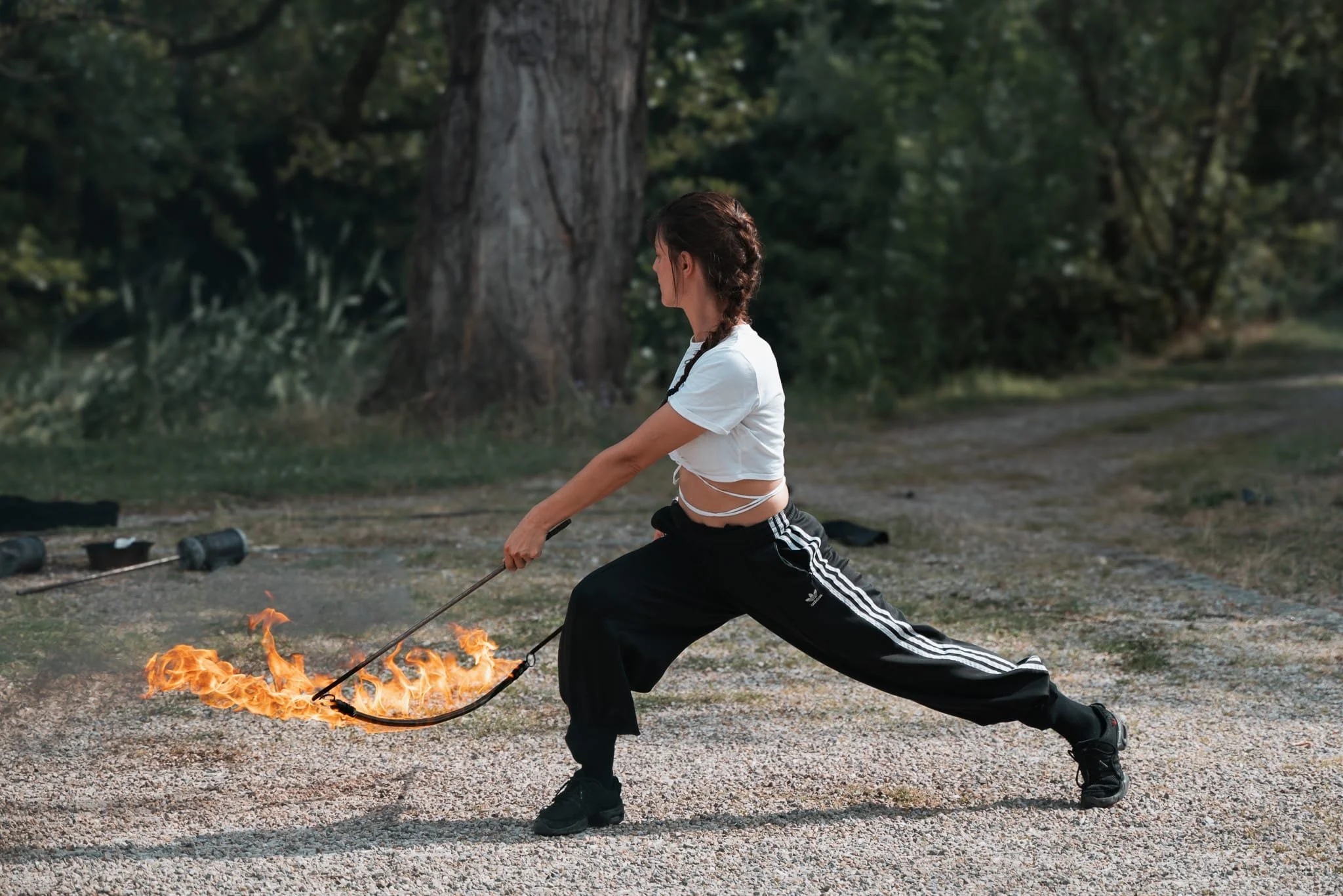 Jeune femme pratiquant le kung-fu avec un bâton en feu dans un environnement extérieur forestier.