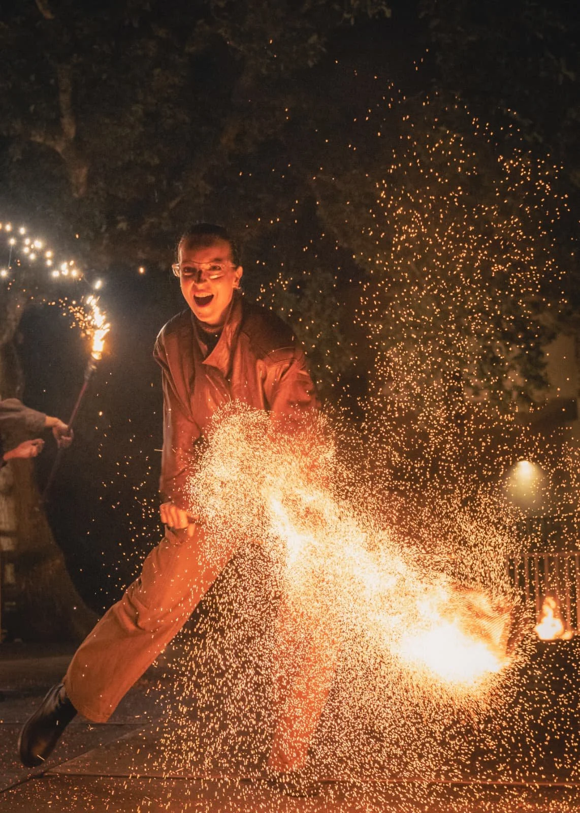 Un homme souriant dansant avec des étincelles lors d'une fête pyrotechnique nocturne.