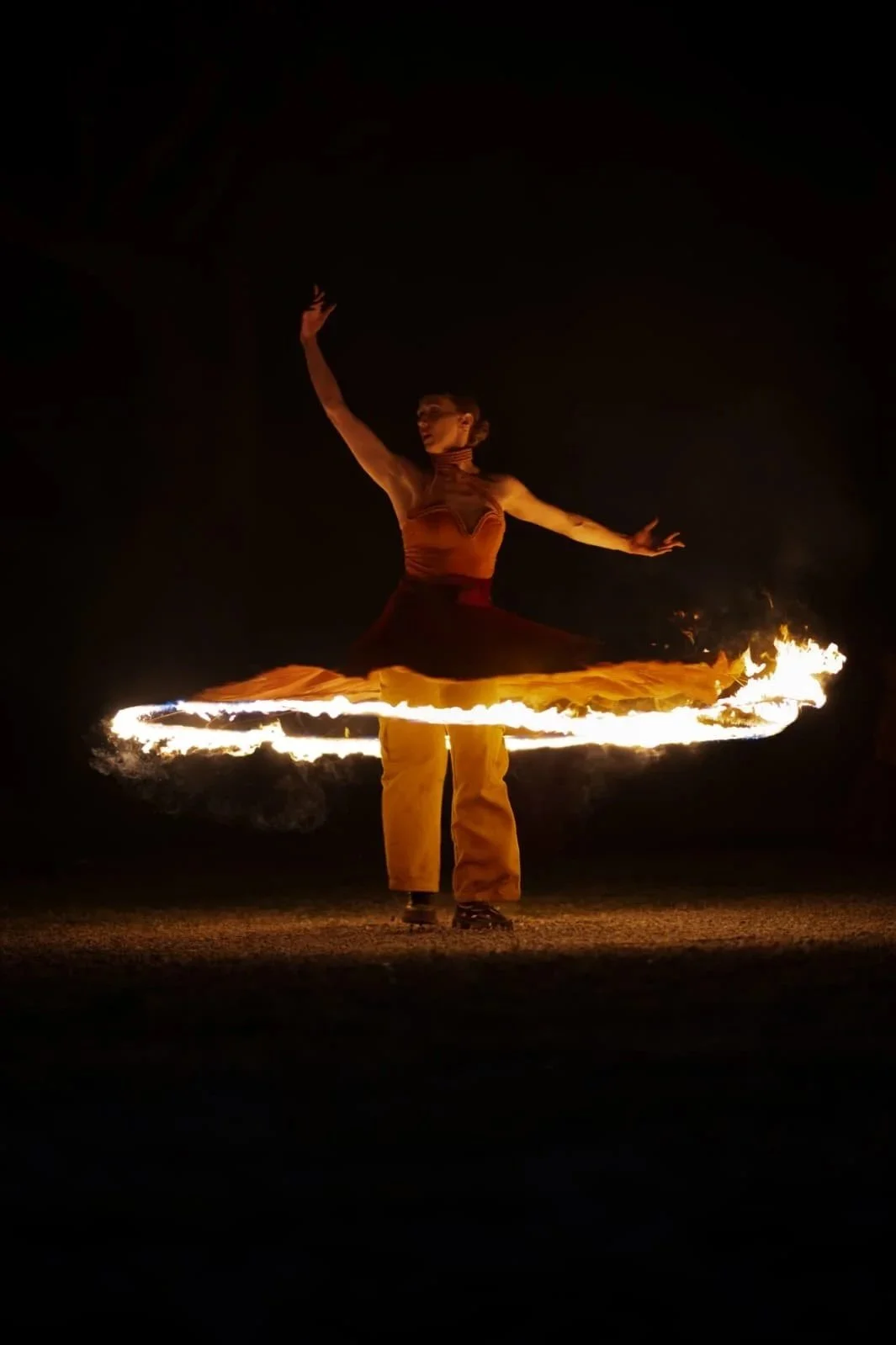 Une danseuse effectuant un spectacle de feu dans l'obscurité, avec un cercle de feu tournant autour d'elle.