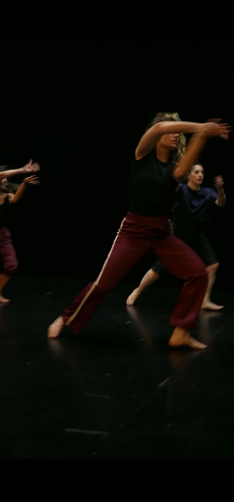 Des danseuses en mouvement lors d'une répétition ou performance de danse contemporaine ou classique dans une salle sombre.