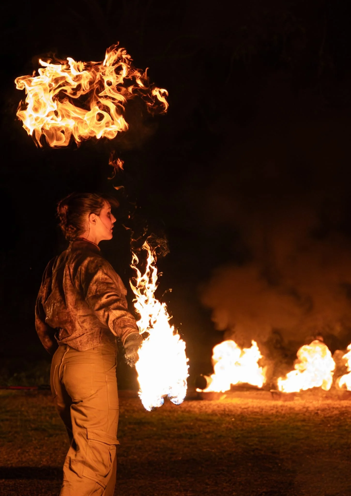 Une femme en tenue beige effectuant un numéro de feu avec des flammes sortant de ses mains, lors d'une performance nocturne.
