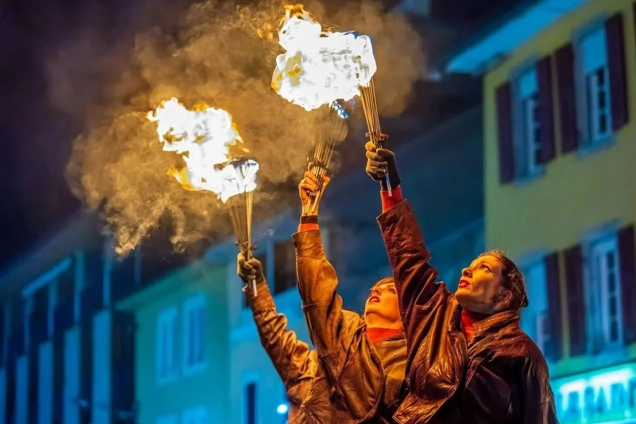 Deux femmes tiennent des torches enflammées lors d'une performance nocturne en ville.