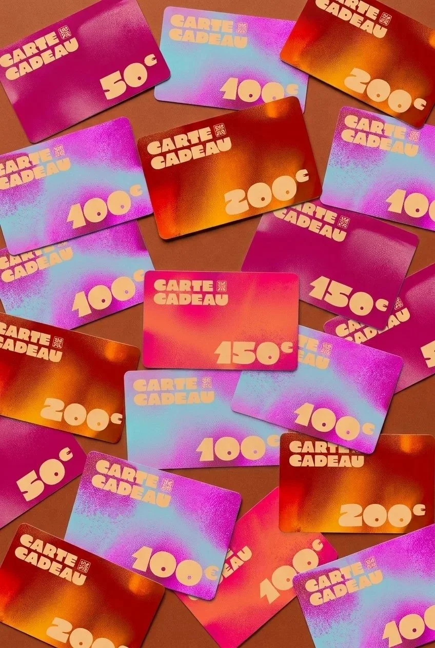 Plusieurs cartes cadeaux de différentes valeurs (50€, 100€, 150€, 200€, 250€) disposées sur une surface. Les cartes sont colorées avec des dégradés de rose, violet, orange et bleu.