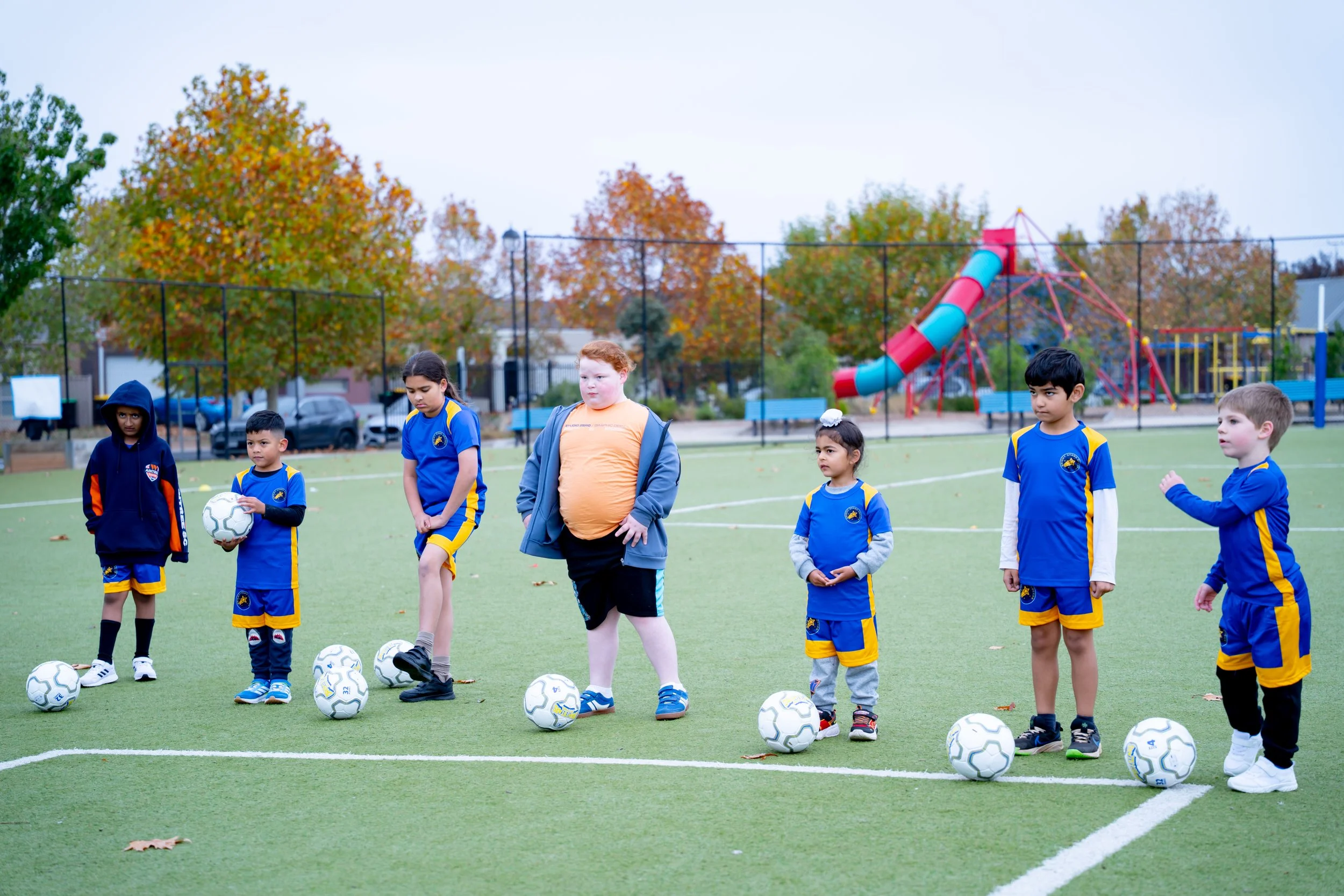 Group of children in Bright Stars Soccer soccer uniforms standing on a green field, lined up with soccer balls in front of them.