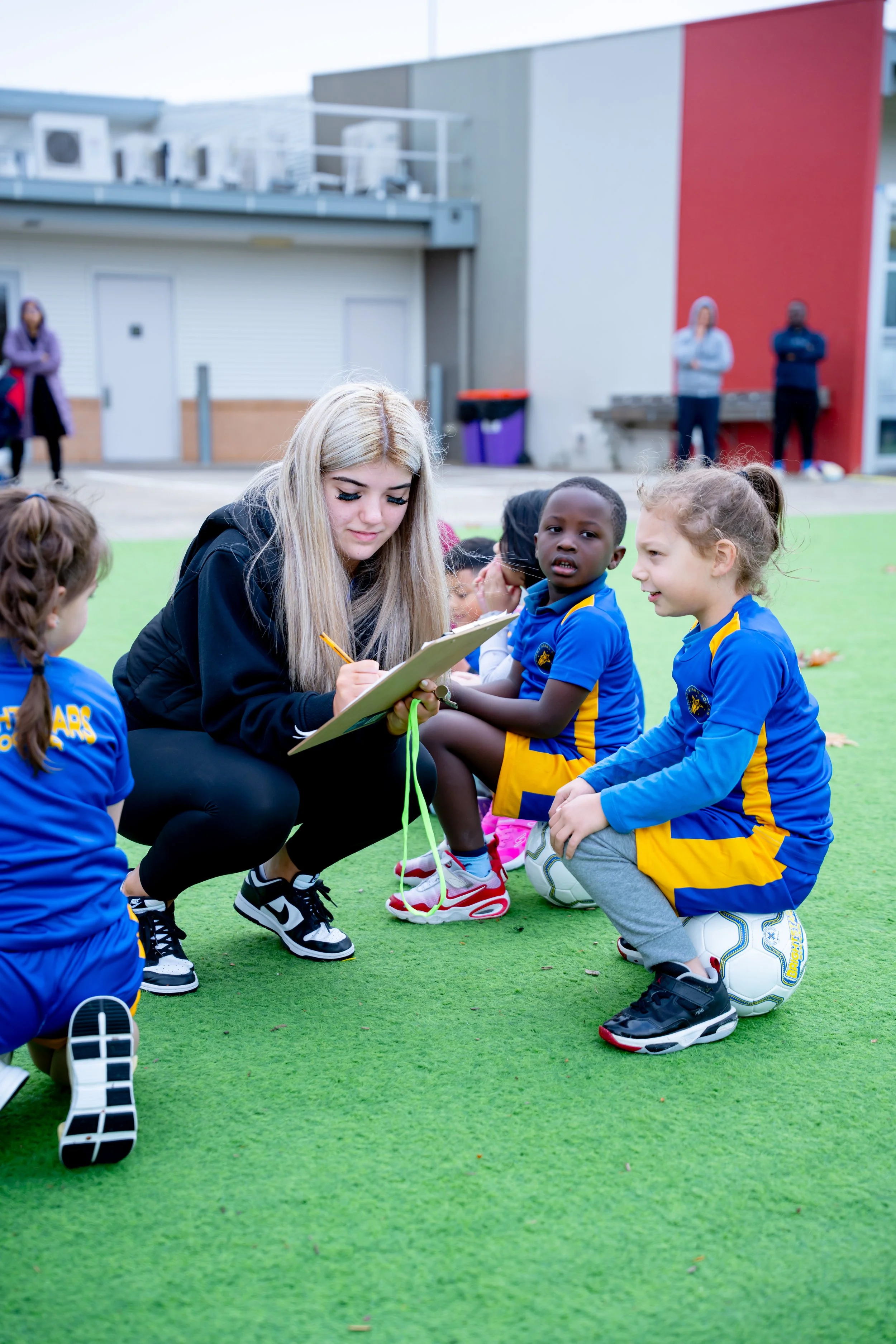 A group of children in blue sports uniforms sitting on the grass in a semi-circle