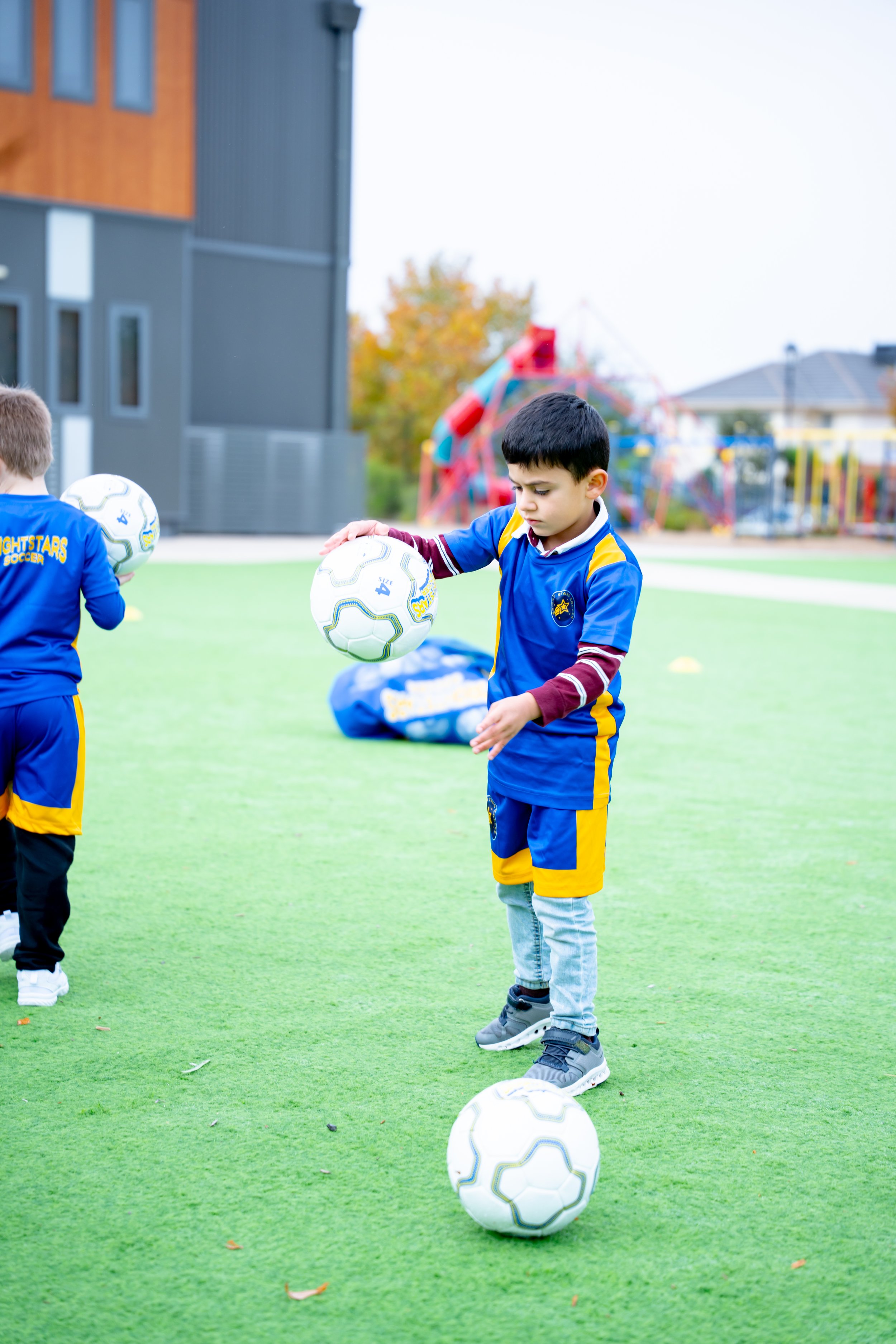 Children in blue and yellow soccer uniforms practicing on a green field with soccer balls