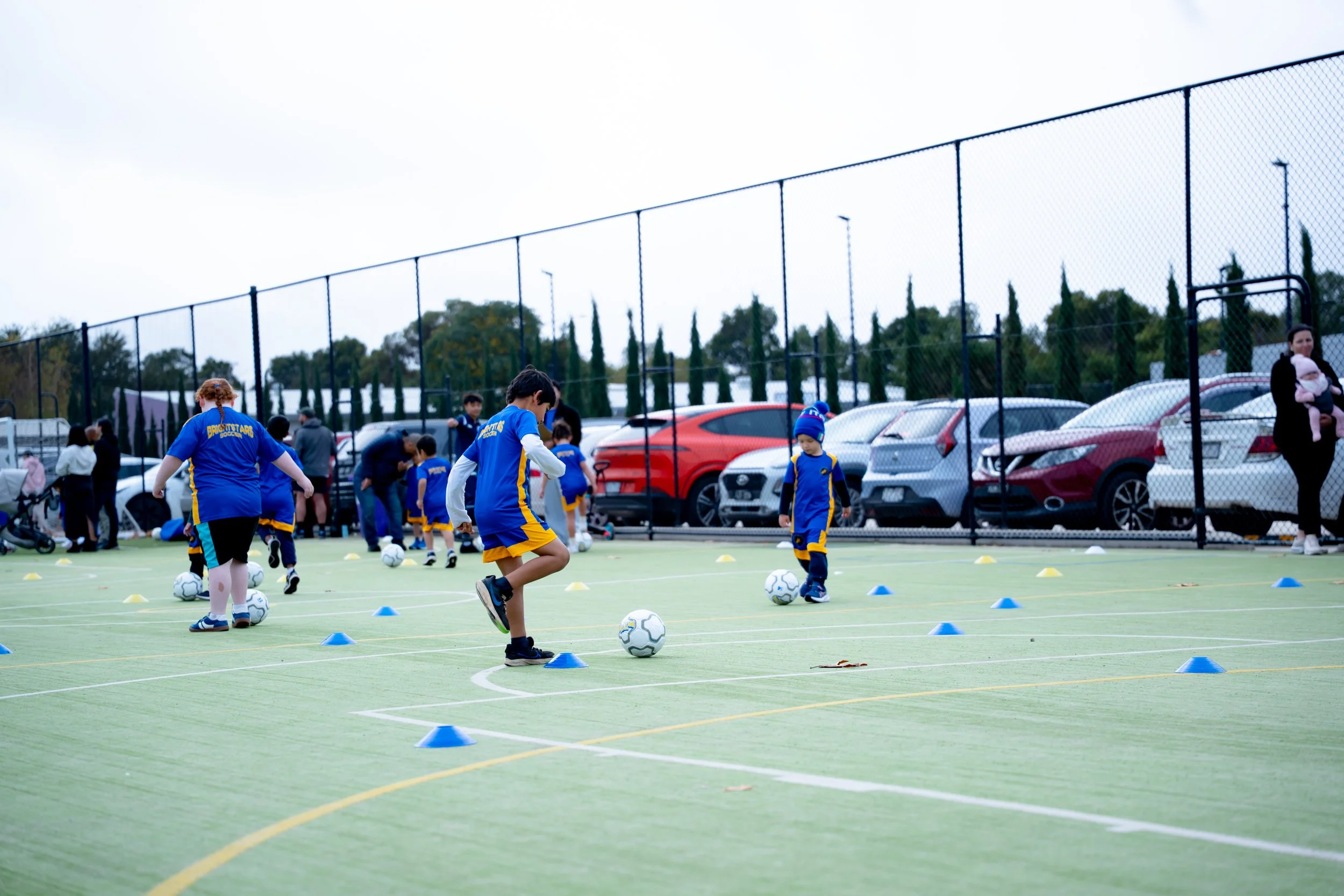 Children in blue and yellow Bright Stars Soccer uniforms practicing dribbling soccer balls around cones.