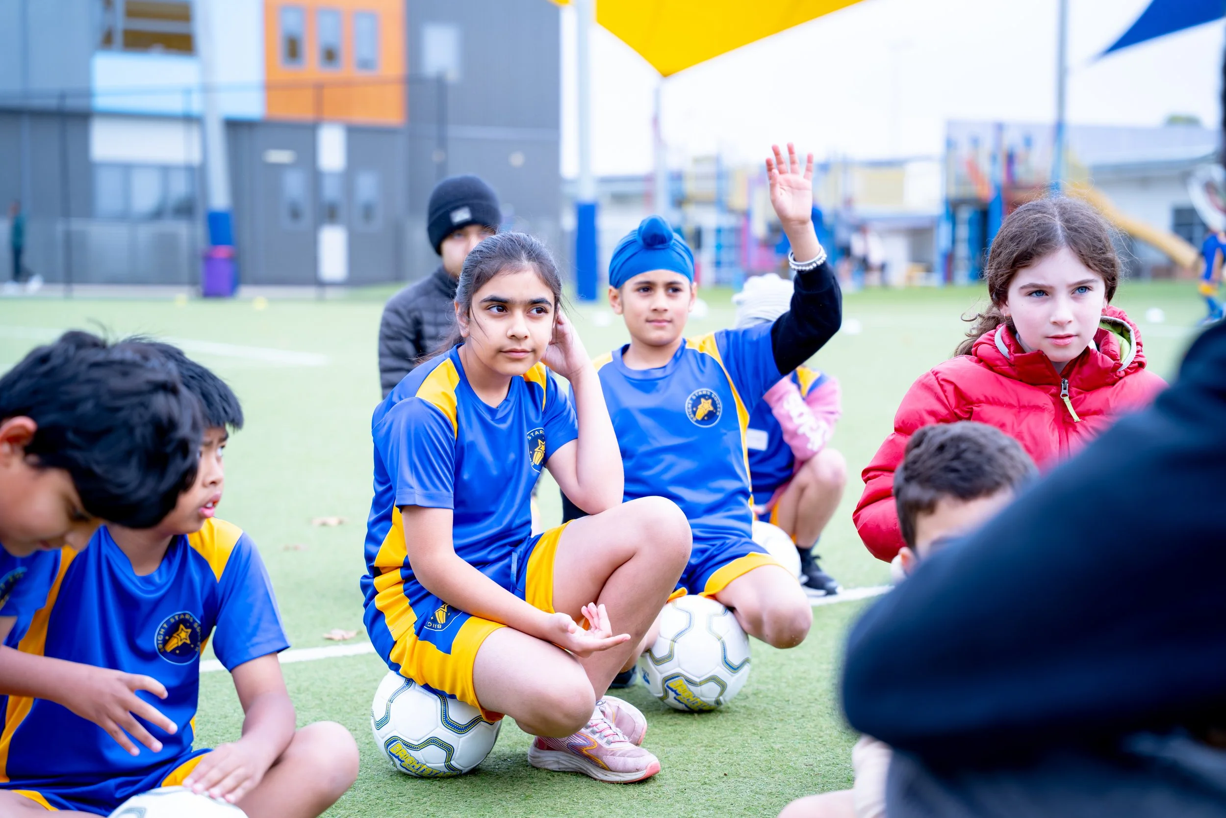 Group of young children sitting on a soccer field during a coaching session
