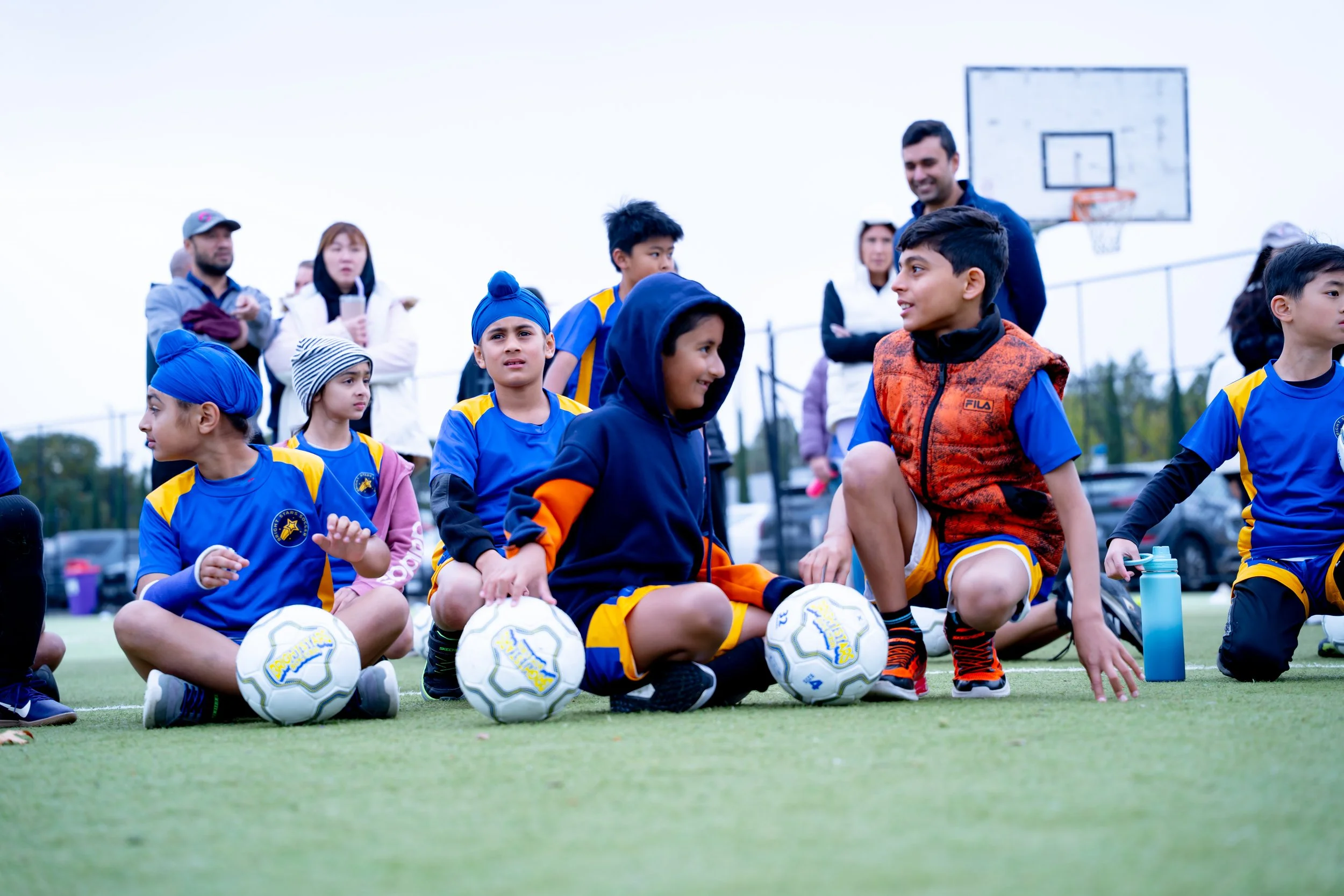 Group of young boys in soccer uniforms sitting on a sports field with their soccer balls