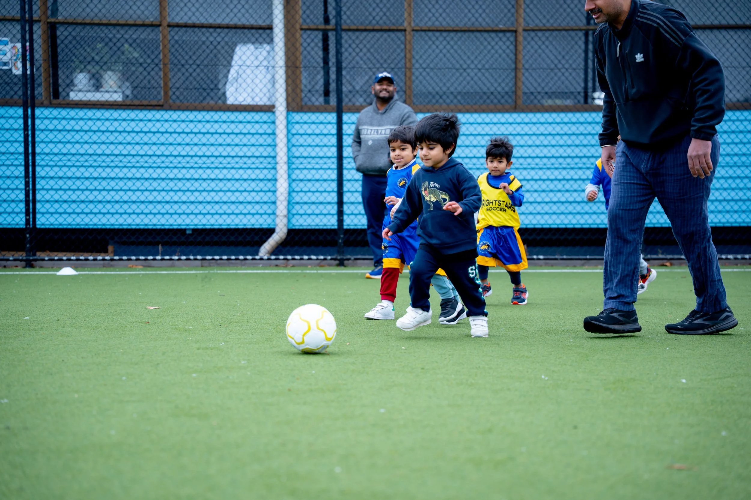 Young children playing soccer on a green field with a coach